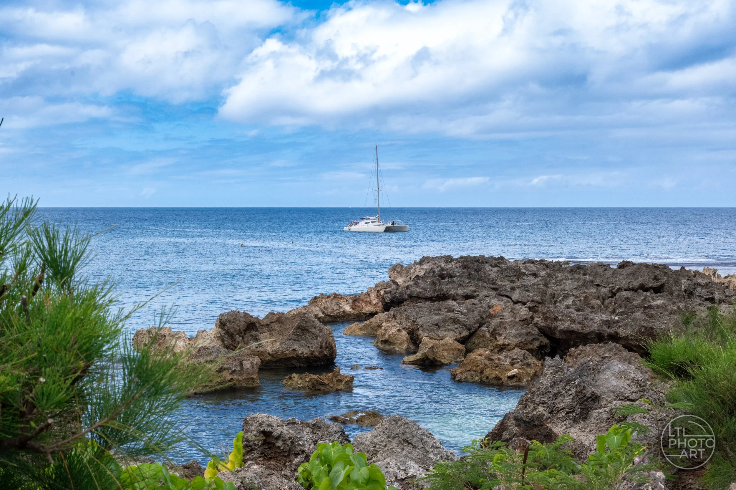 White catamaran anchored beyond a rocky shoreline at Haleʻiwa Beach Park on the North Shore of Oahu, Hawaii.