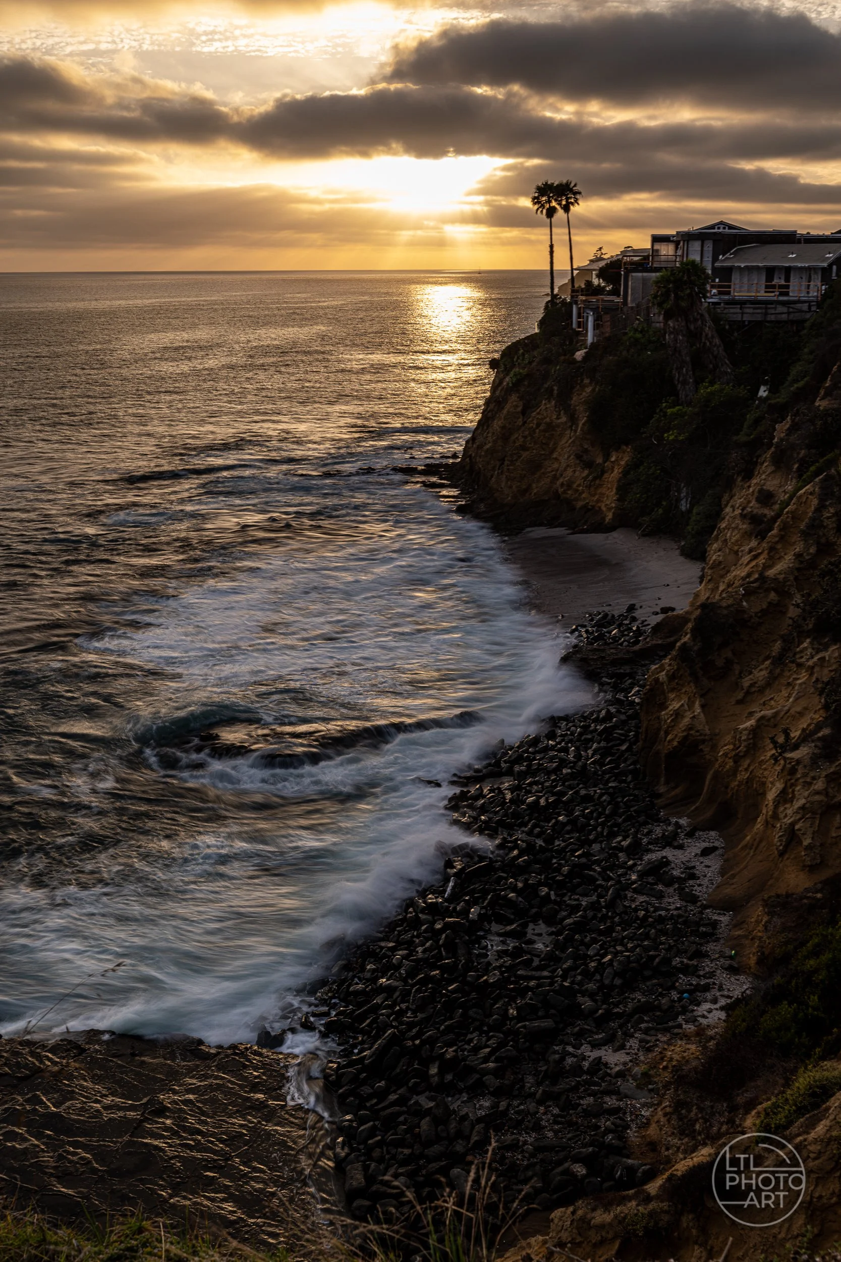 Sunset rays and golden reflections over the Pacific with soft waves along the rocky Laguna Beach shoreline.