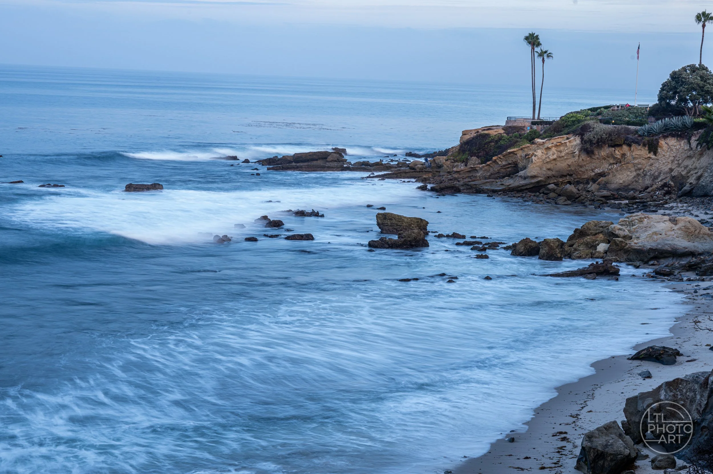 Slow-shutter blue-hour view of waves, rocks, and Monument Point from an elevated position in Heisler Park, Laguna Beach.