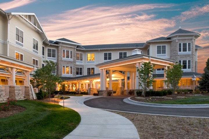 Large multi-story residential building with a curved driveway, landscaped greenery, and a covered entrance at sunset.