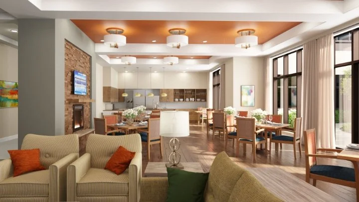 Open-concept living and dining area with beige sofas, orange accent pillows, multiple dining tables with chairs, large windows with curtains, and a kitchen in the background.