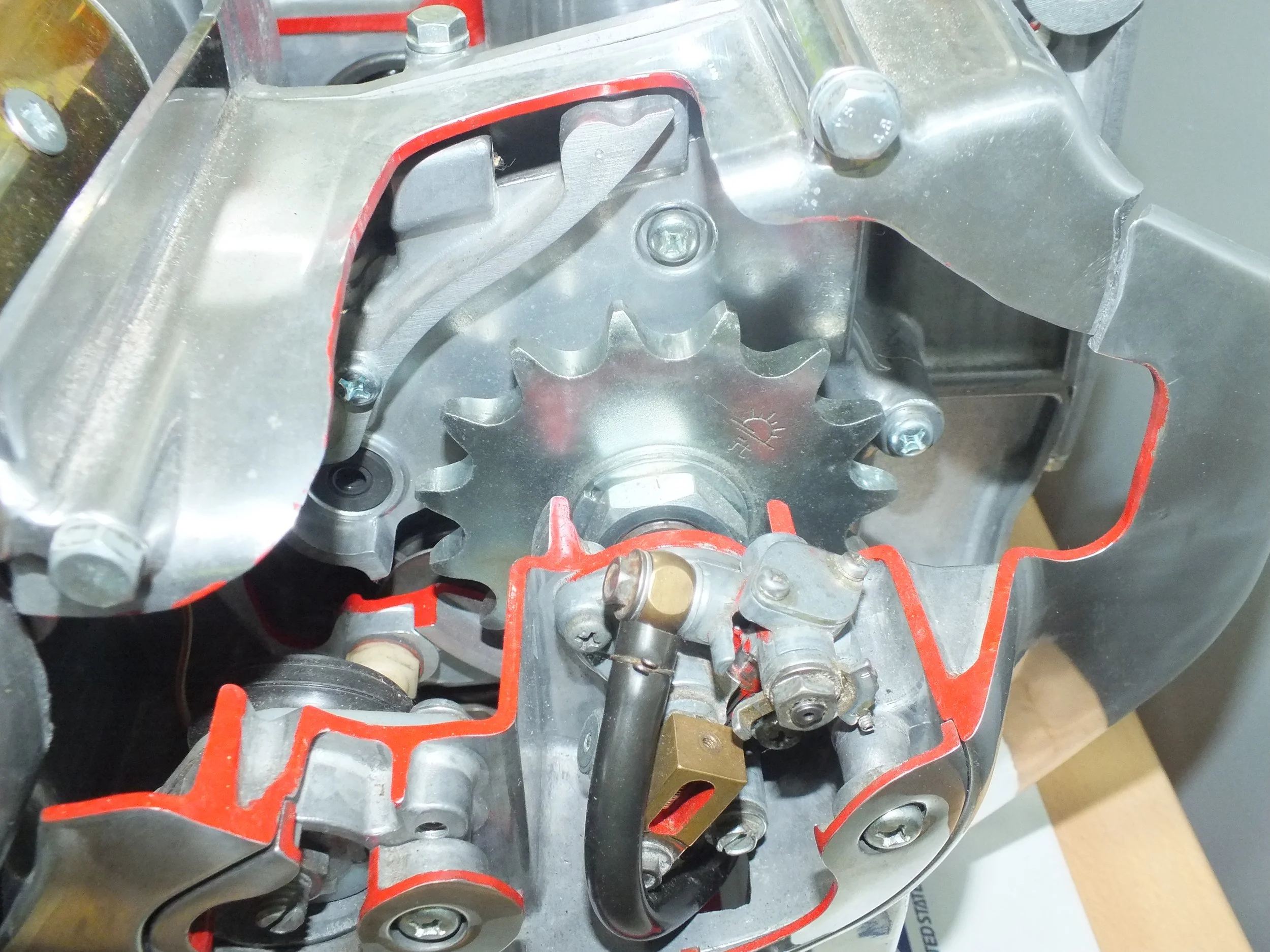 Close-up view of a metallic engine component with red gasket material and various bolts.