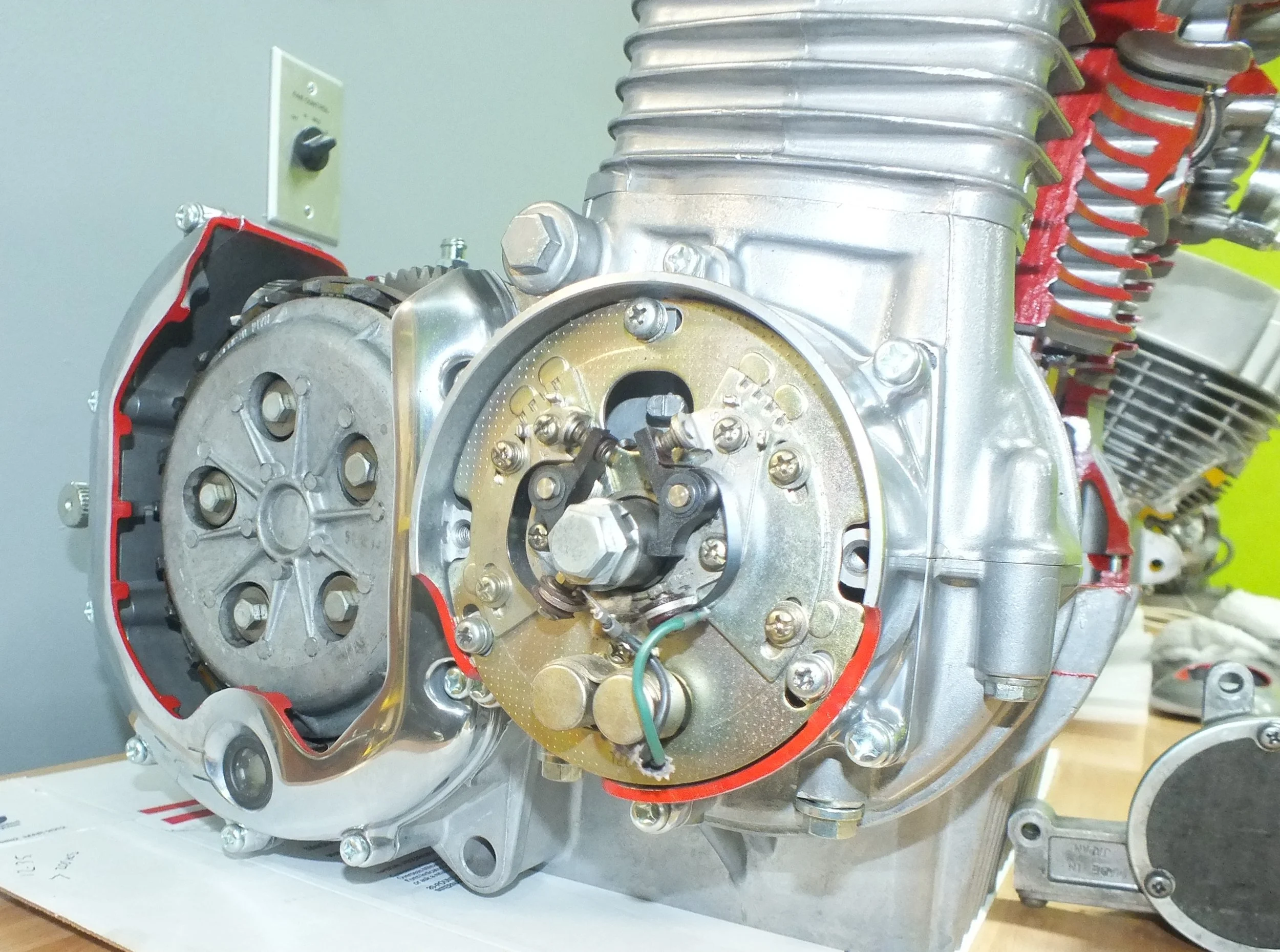 Close-up of a mechanical engine component, showing metal parts, screws, and wires, mounted on a surface with a yellow and gray background.