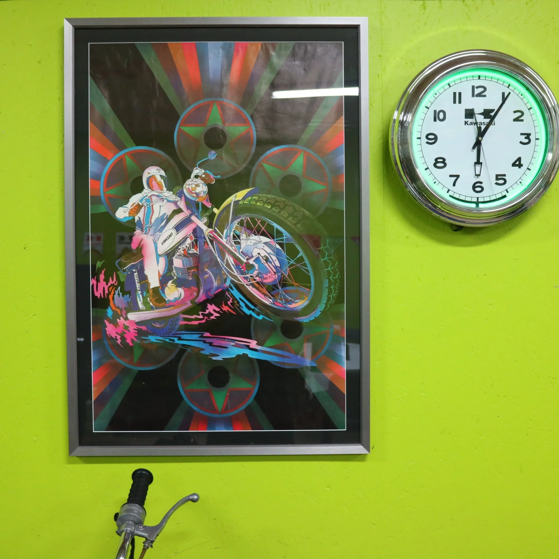 Colorful poster featuring a person riding a bicycle, with red and green star designs in the background, mounted on a lime green wall. To the right, a round wall clock showing the time as 1:05.