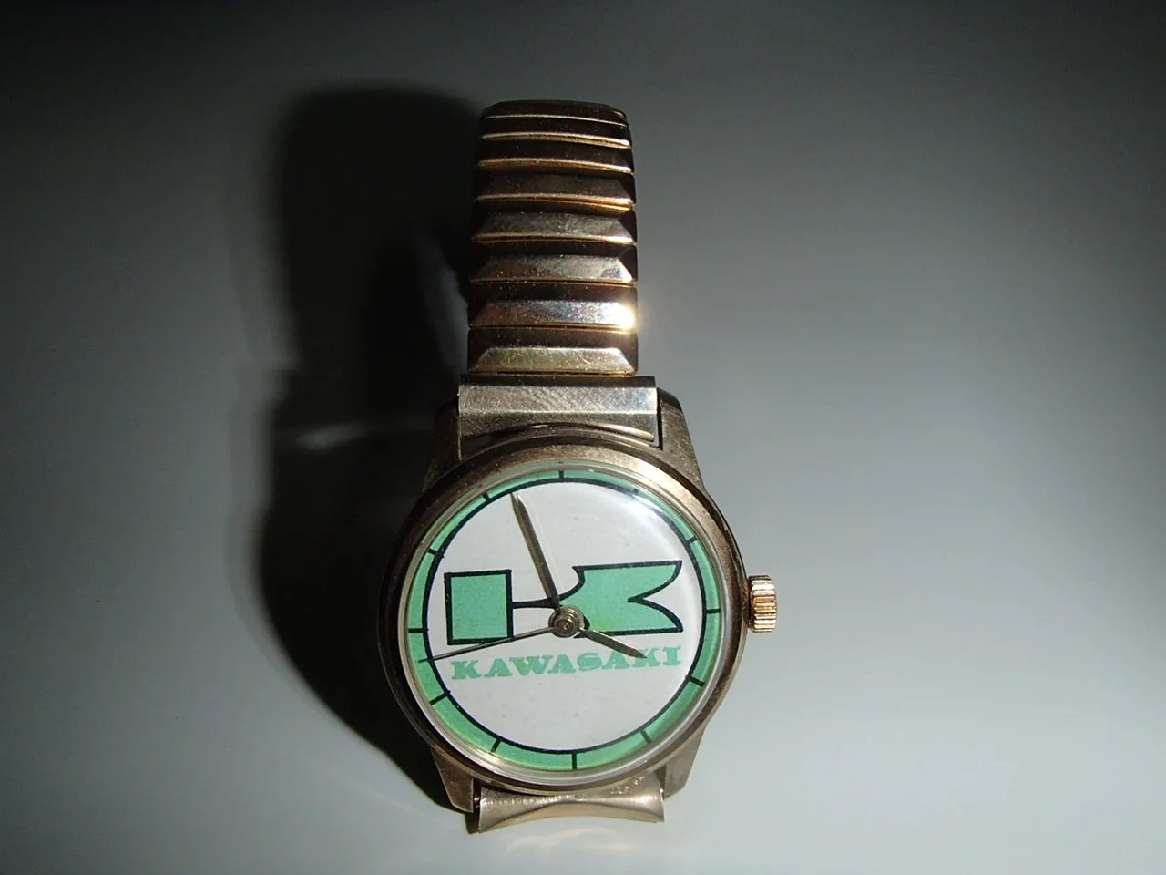 A wristwatch with a silver metal band displaying a manga-style cartoon face with large green eyes, a black nose, and the word 'KAWASAKI' underneath.