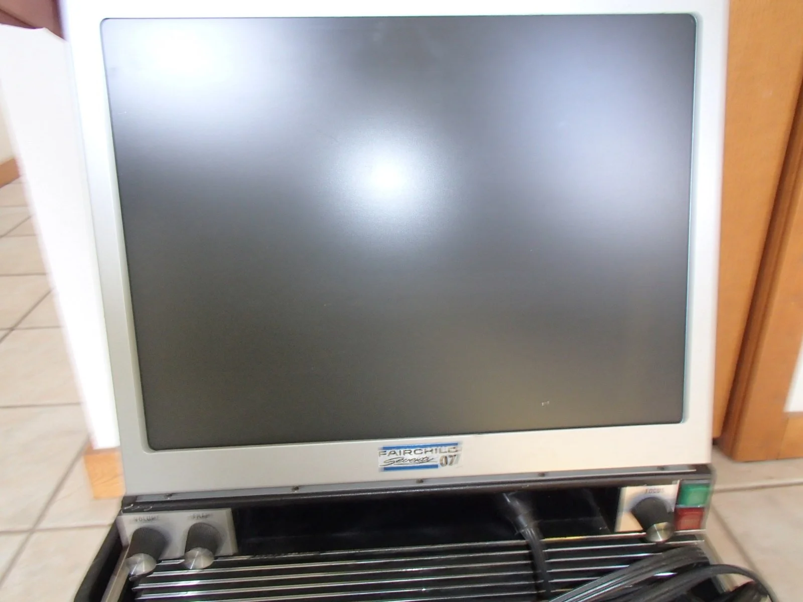 An old medical monitor with a blank screen, part of a vintage medical diagnostic machine, on a tiled floor.