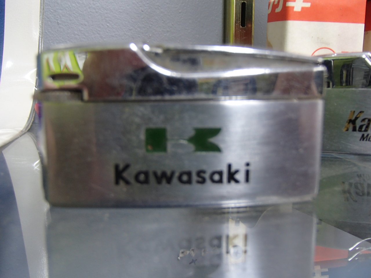 A silver metal lighter with the Kawasaki logo and name printed on it.