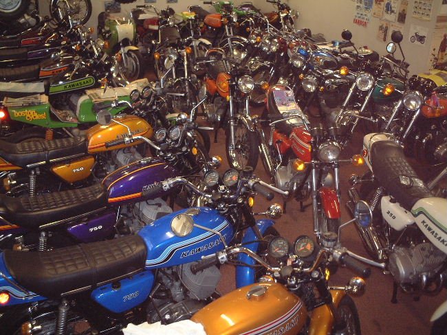 Multiple vintage motorcycles and bikes parked indoors.