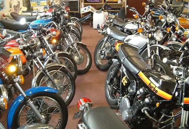 A collection of vintage motorcycles in a showroom or garage, with various models lined up closely together.