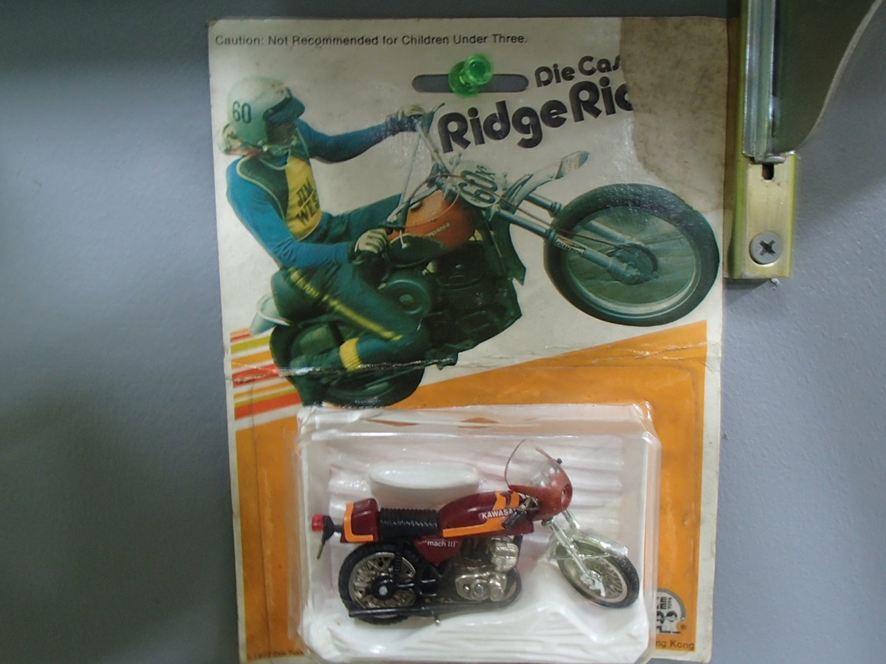 A vintage motorcycle toy in its original packaging attached to a Ridge Rider bike poster.