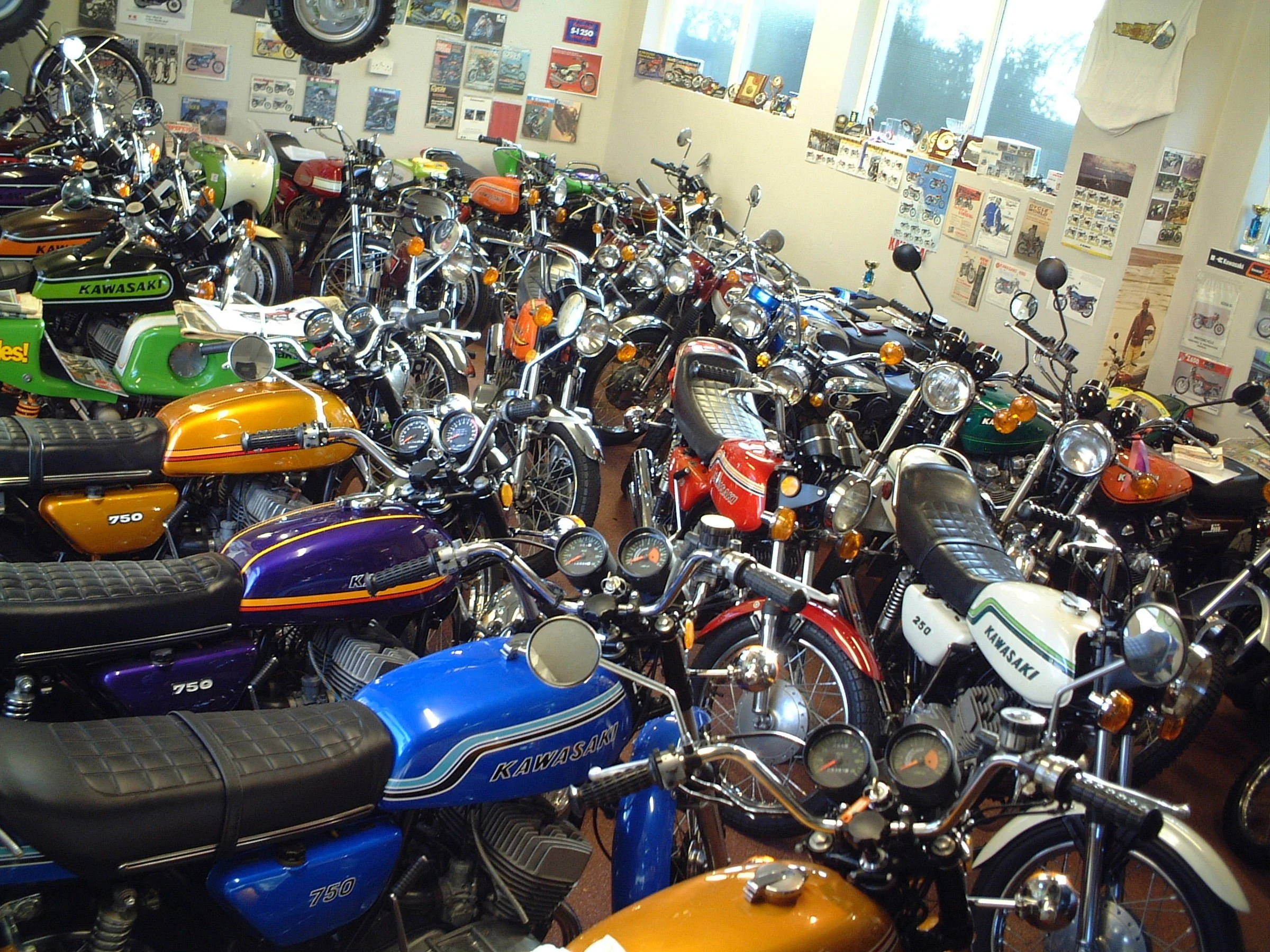 A room filled with vintage Kawasaki motorcycles, with posters and model displays on the walls and several motorcycles parked inside.