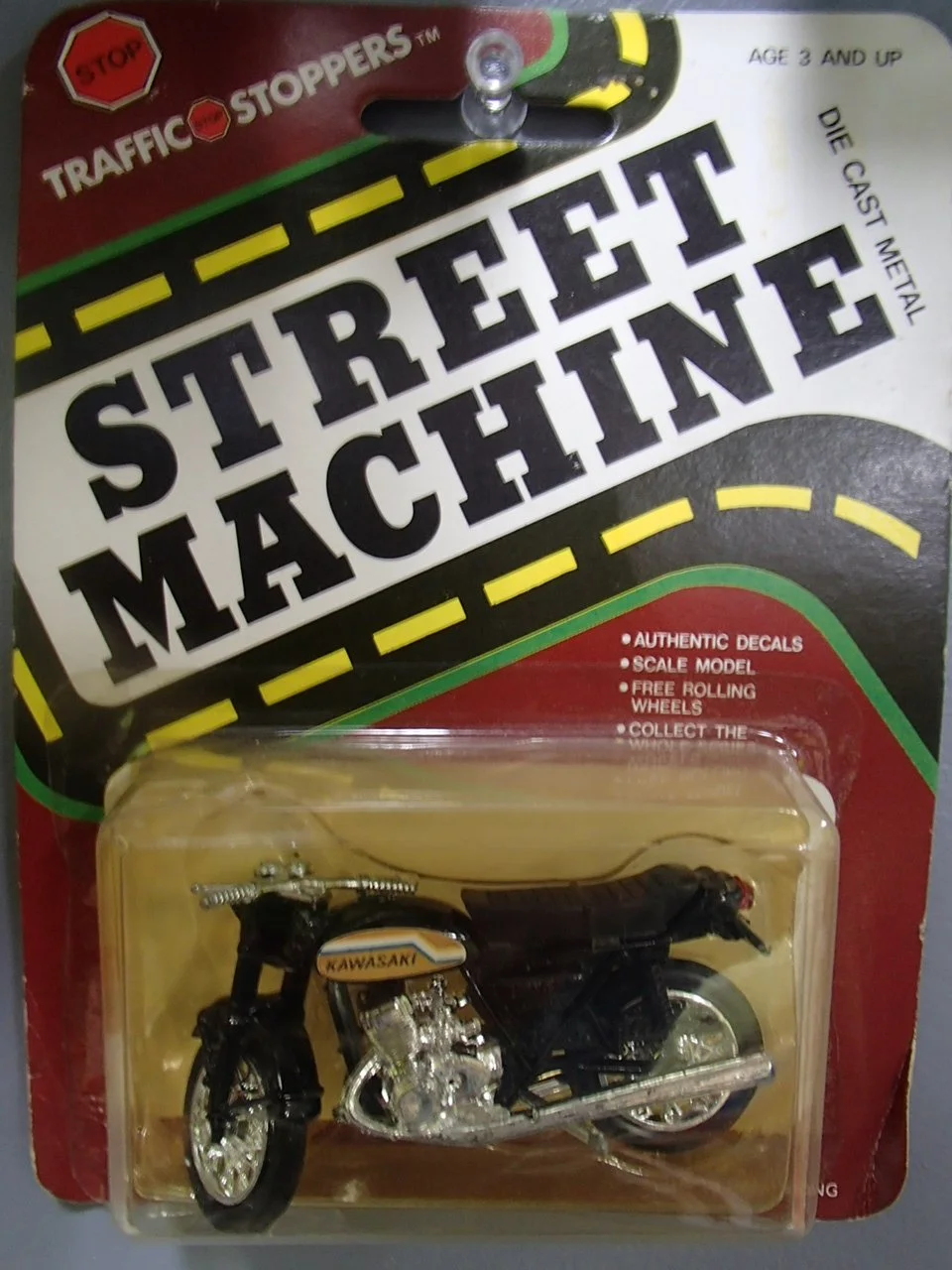 A die-cast metal toy motorcycle with a black body and silver engine, packaged in clear plastic with a cardboard backing that reads 'Street Machine' and 'Traffic Stoppers'.