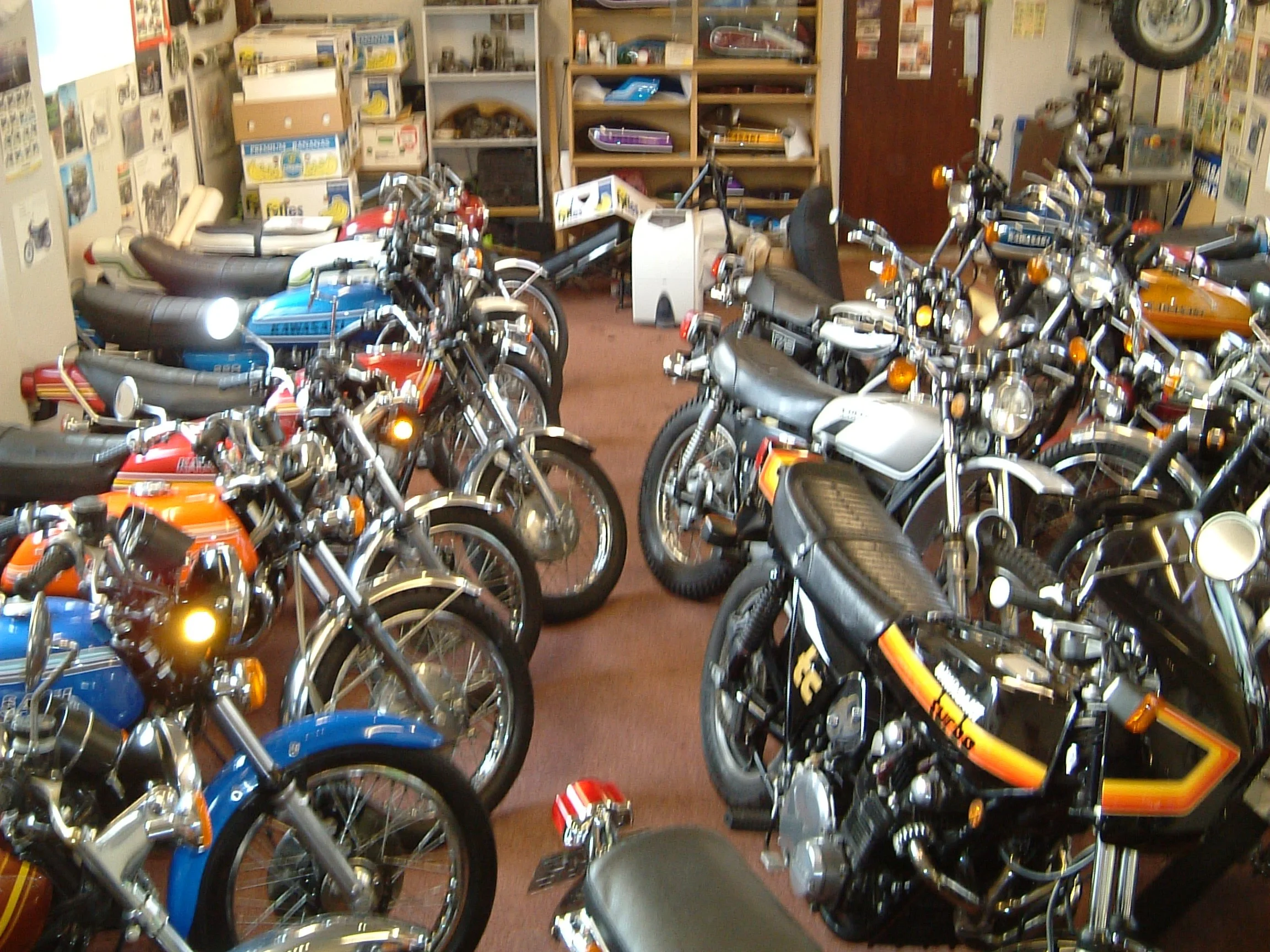 A room with multiple parked motorcycles and motorcycles on shelves, with boxes and various items on shelves in the background.