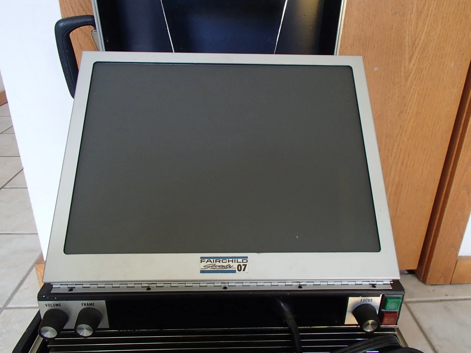 A vintage Fairchild vacuum tube heat press machine with a digital control panel, knobs, and a flat heating surface, placed on a tiled floor next to a wooden cabinet.