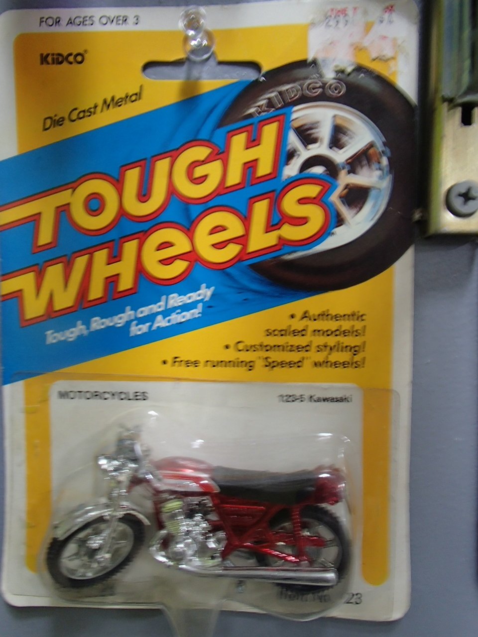 A Kidco die-cast metal motorcycle toy in red, packaged in a yellow and blue display card with the 'Tough Wheels' logo, designed for children over 3 years old.
