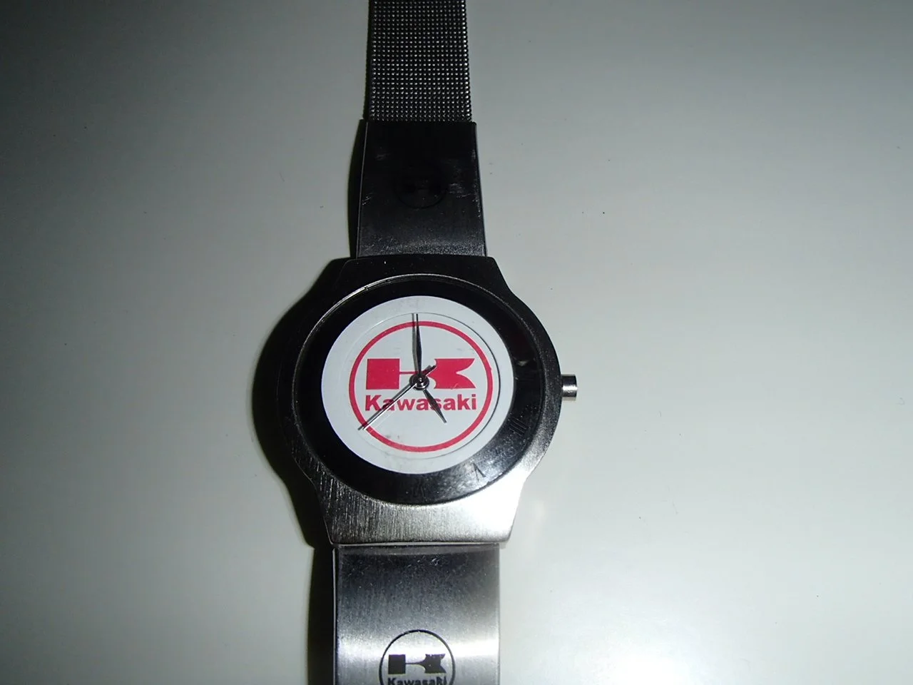 A wristwatch with a black bezel and metal band displaying the Kawasaki logo and text on the face.