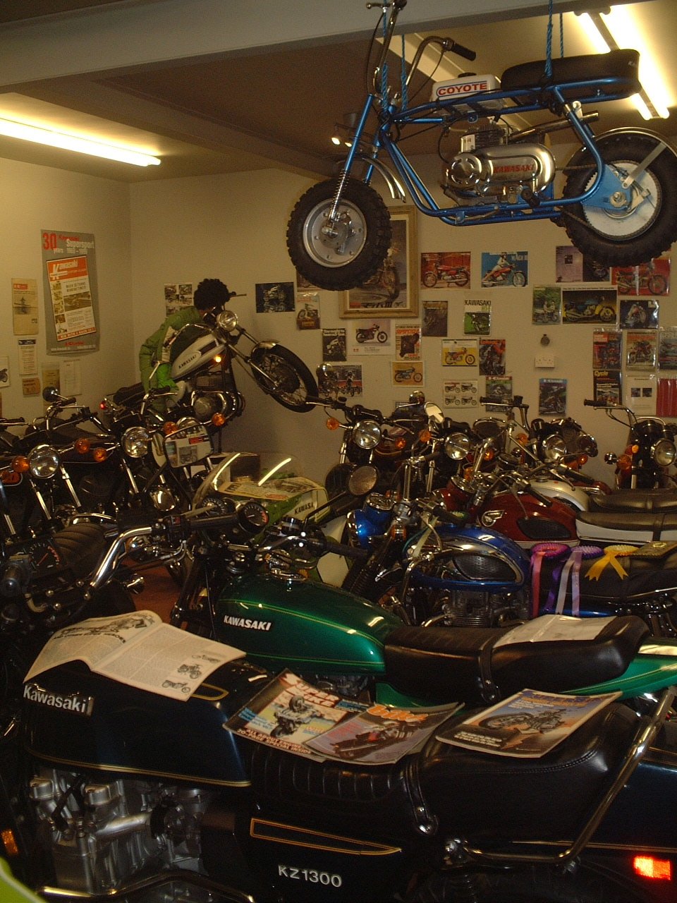 Collection of vintage Kawasaki motorcycles and a blue minibike displayed on the ceiling in a museum or showroom.