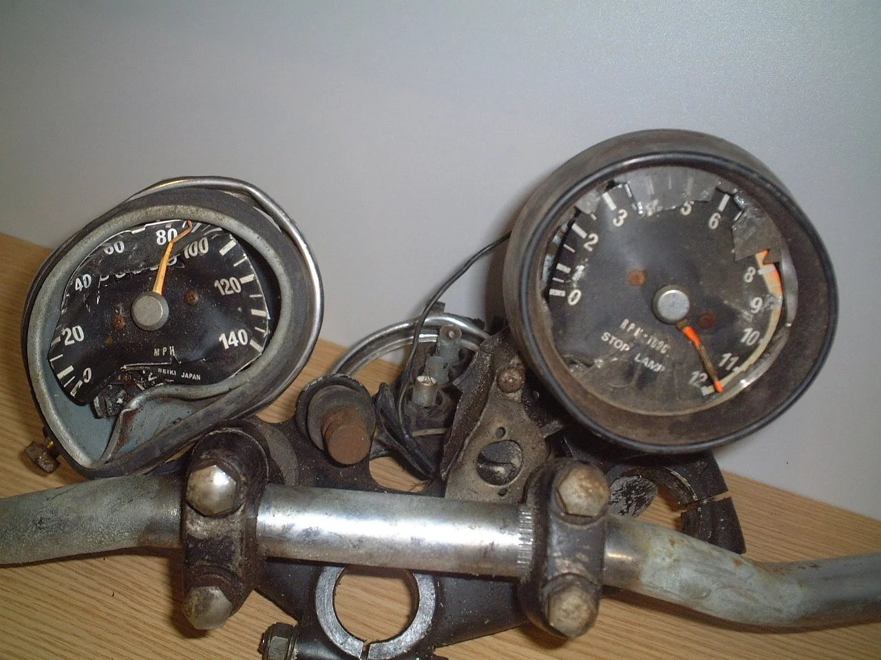 A photo of vintage motorcycle gauges, including a speedometer and a tachometer, mounted on a rusty metal frame.