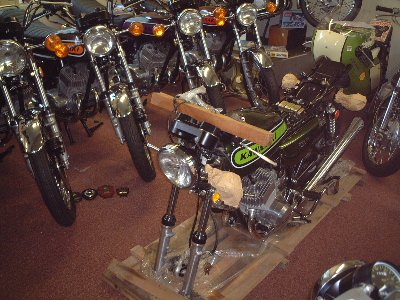 A motorcycle on a wooden pallet surrounded by several other motorcycles in a showroom or garage.