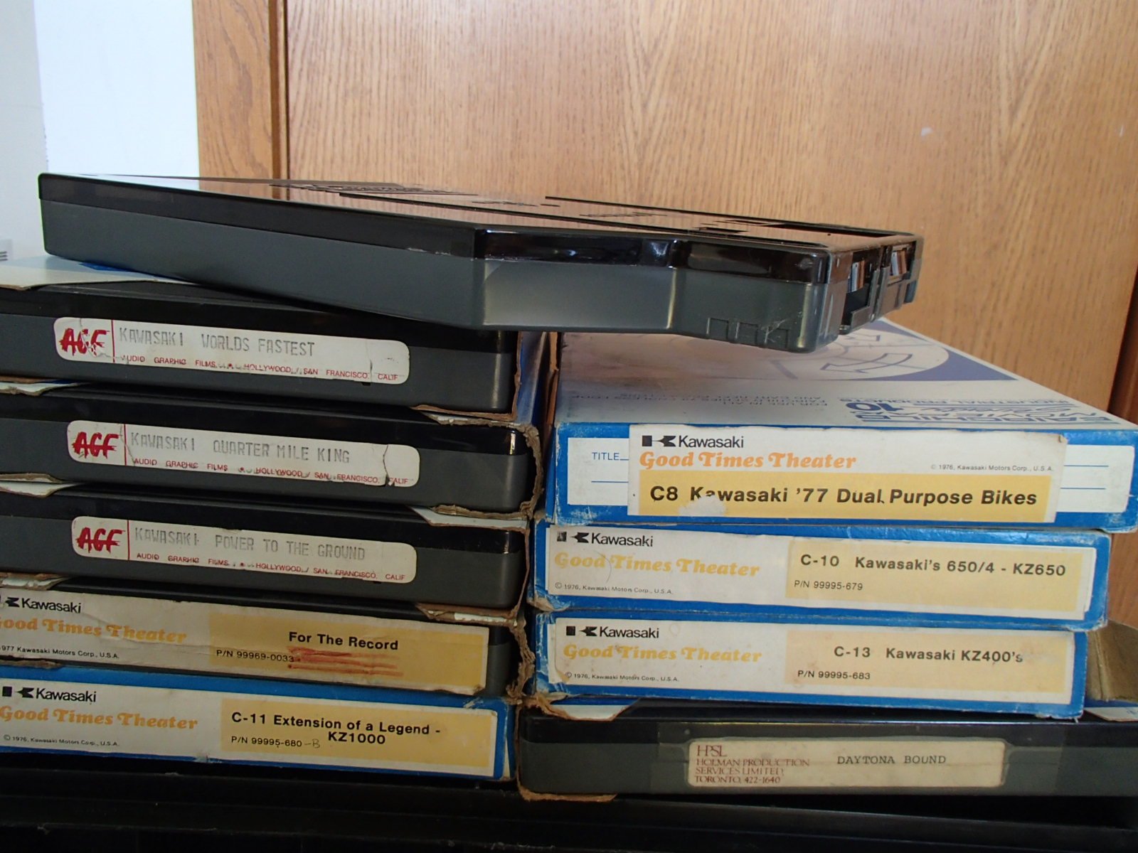 Stack of vintage audio tape boxes, including titles related to Kawasaki motorcycles and bands, with some labels reading 'Good Times Theater' and 'For The Record'.