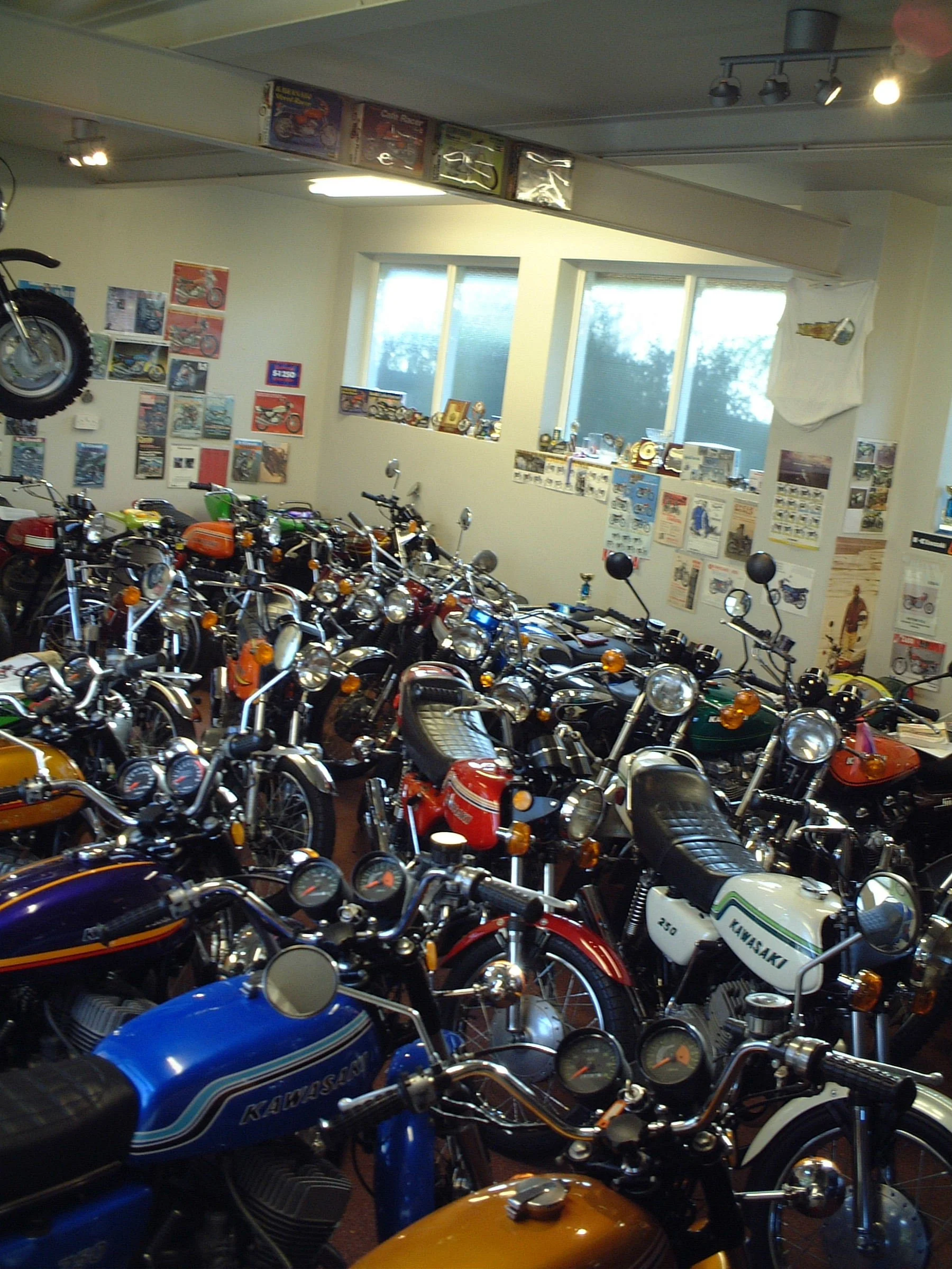 A collection of vintage motorcycles and scooters inside a room with posters on the walls and windows.