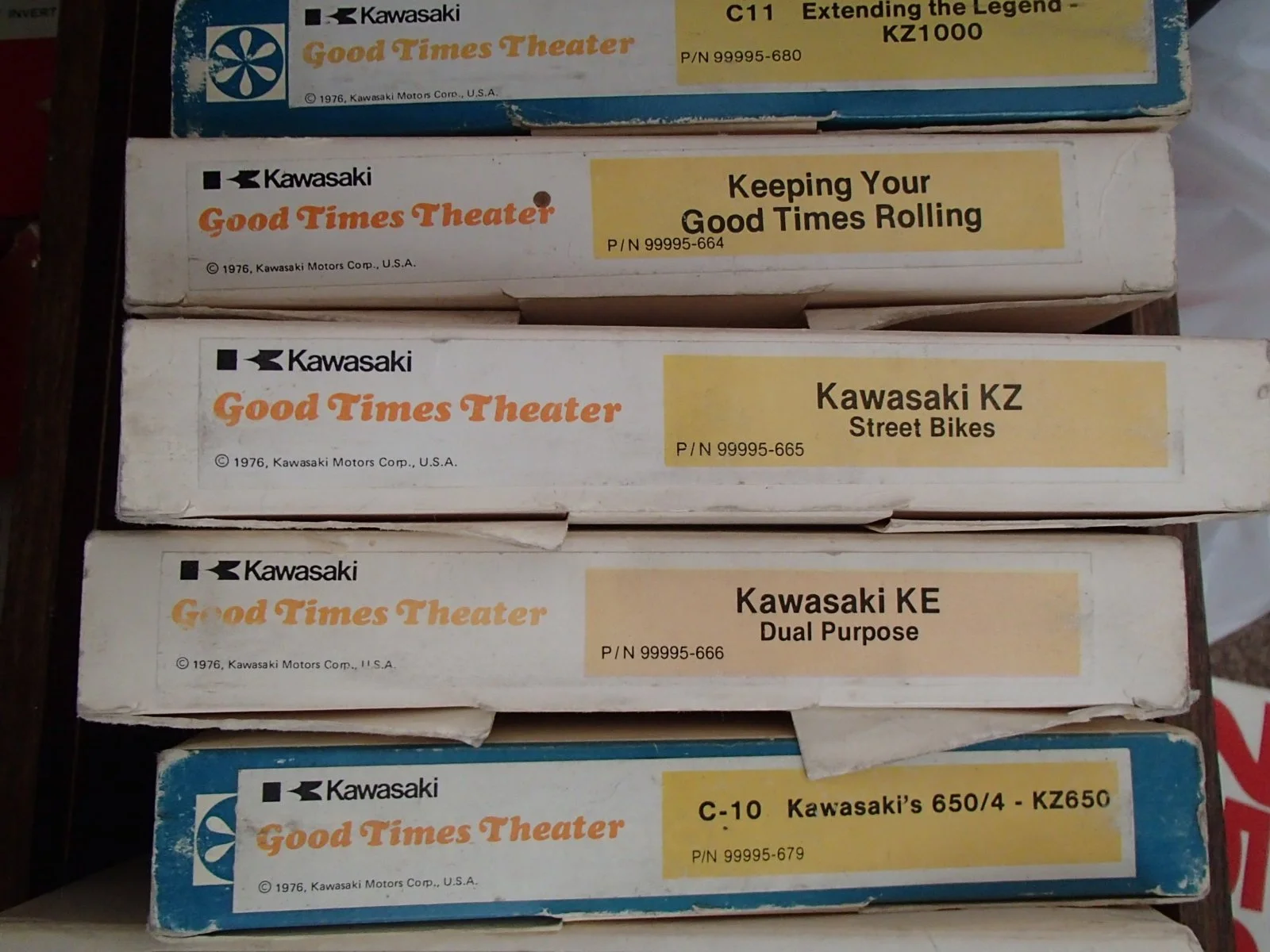 Stacked vintage Kawasaki toy motorcycle boxes with labels reading 'Good Times Theater' and details about different Kawasaki motorcycle models from 1976.