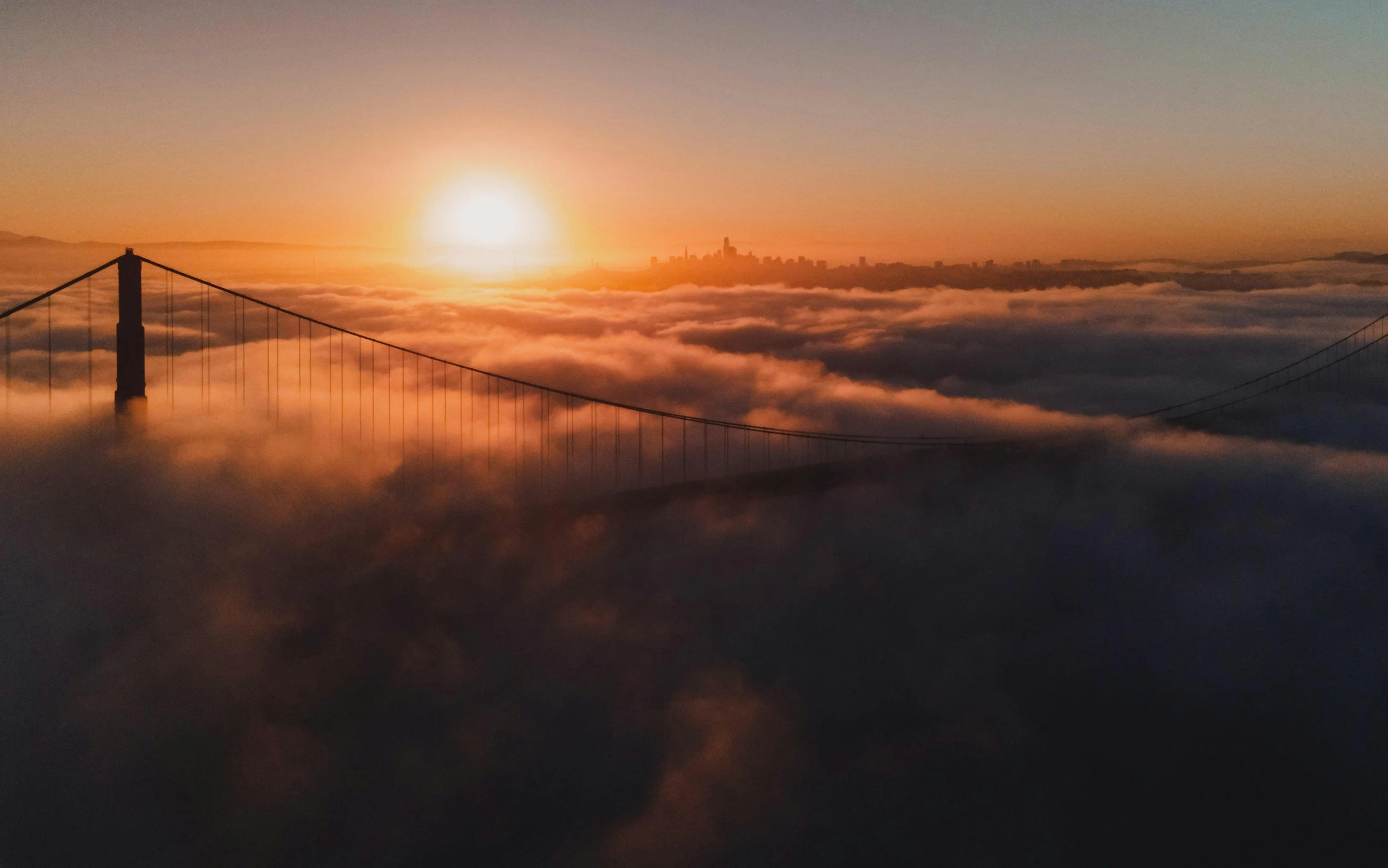 Sunrise over San Francisco skyline with clouds below Golden Gate Bridge