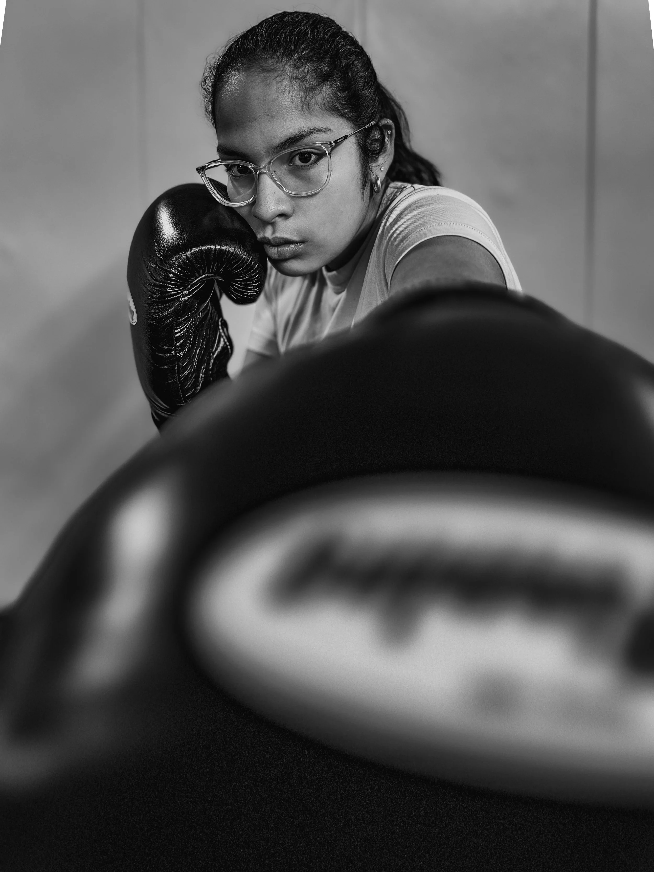A woman in glasses wearing boxing gloves and looking directly at the camera, black and white photo.
