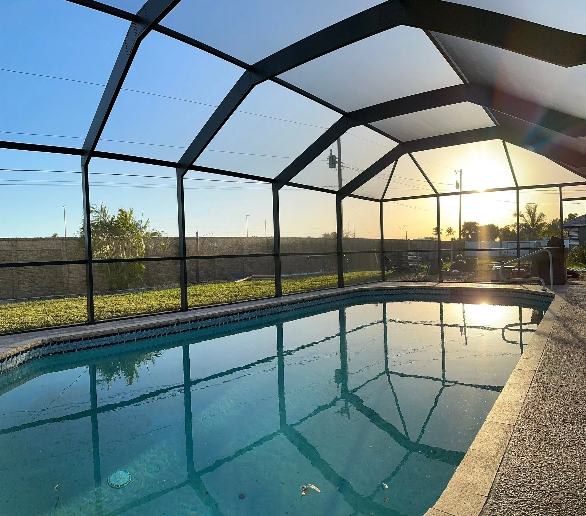 Completed pool cage restoration with newly painted aluminum framing and professionally installed screen panels around a residential swimming pool.