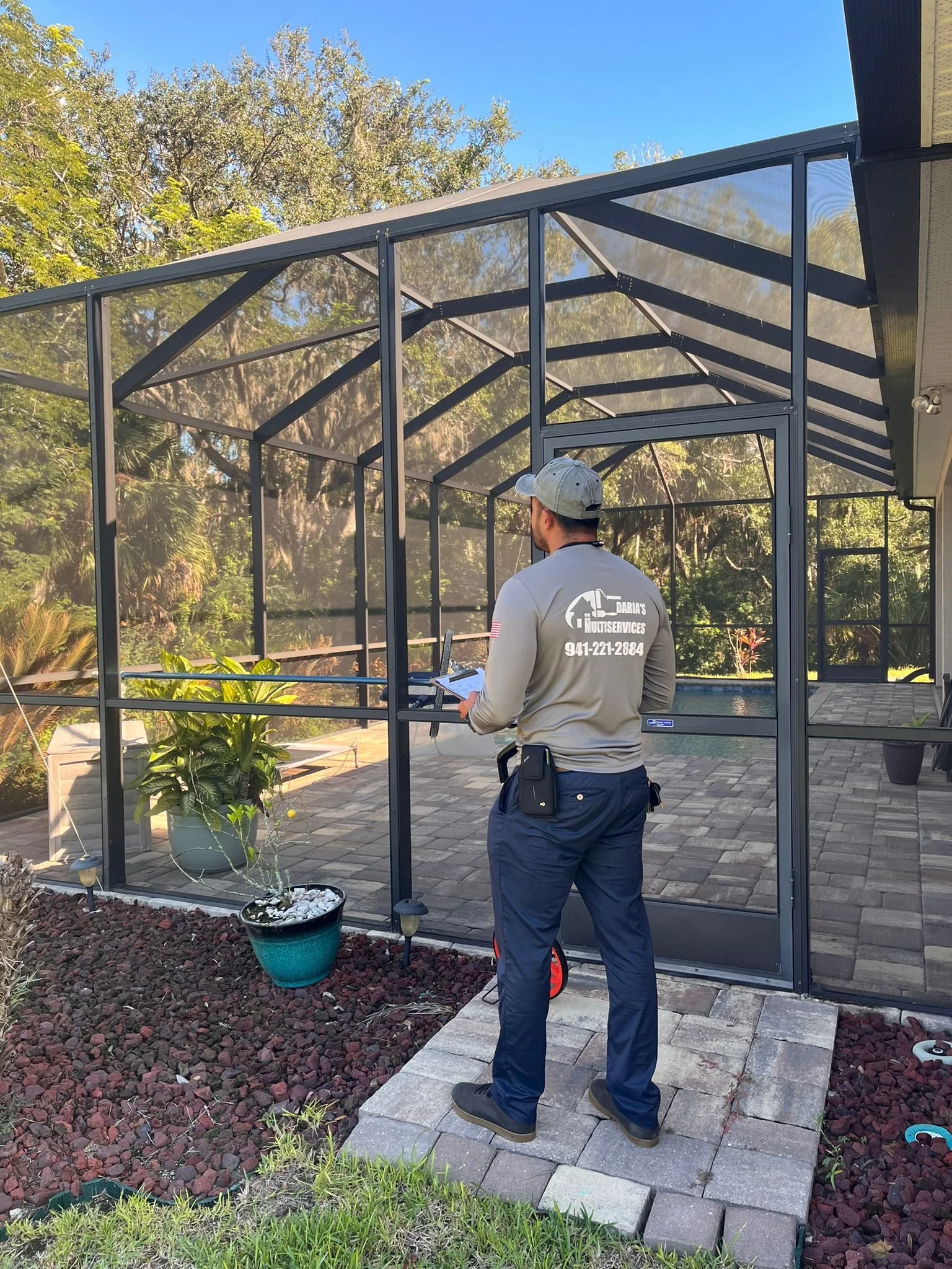 Technician performing an on-site inspection of a pool cage enclosure before restoration and rescreening services.