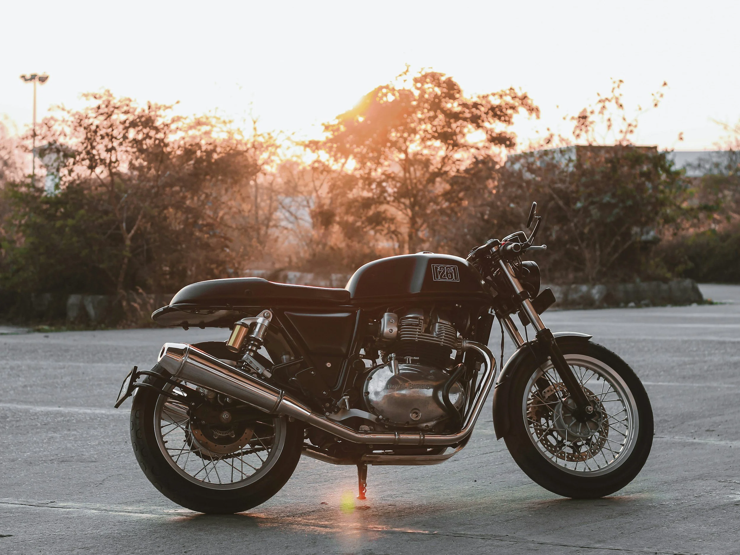 Black motorcycle parked on an empty parking lot at sunset, with trees and a building in the background.