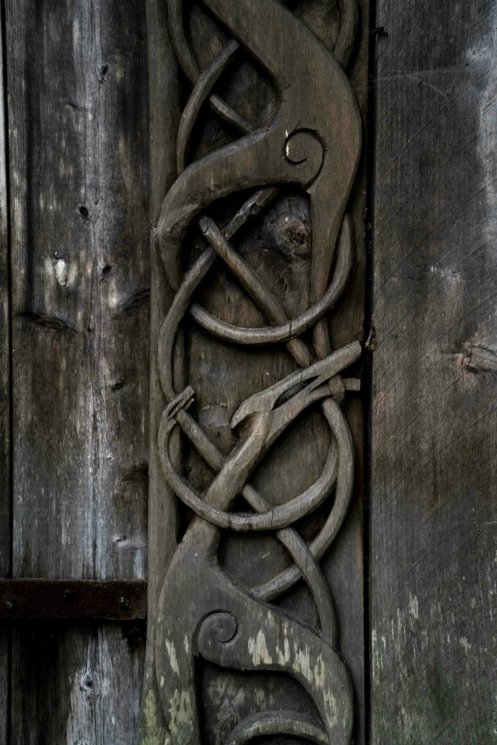 A carved wooden totem pole with intricate designs, mounted on a weathered wooden wall.