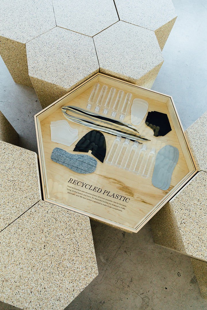 Display of various recycled plastic items, including test tubes, face masks, socks, and strips, on a wooden octagonal table with a label that reads 'Recycled Plastic.'
