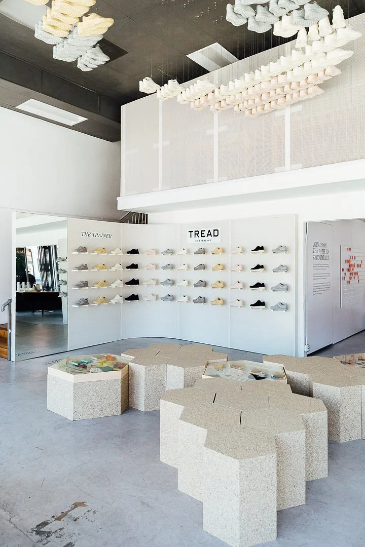 Display of shoes on white wall with 'TREAD BY SKECHERS' sign in a modern retail store, with unique hexagonal seating arrangements in the foreground.