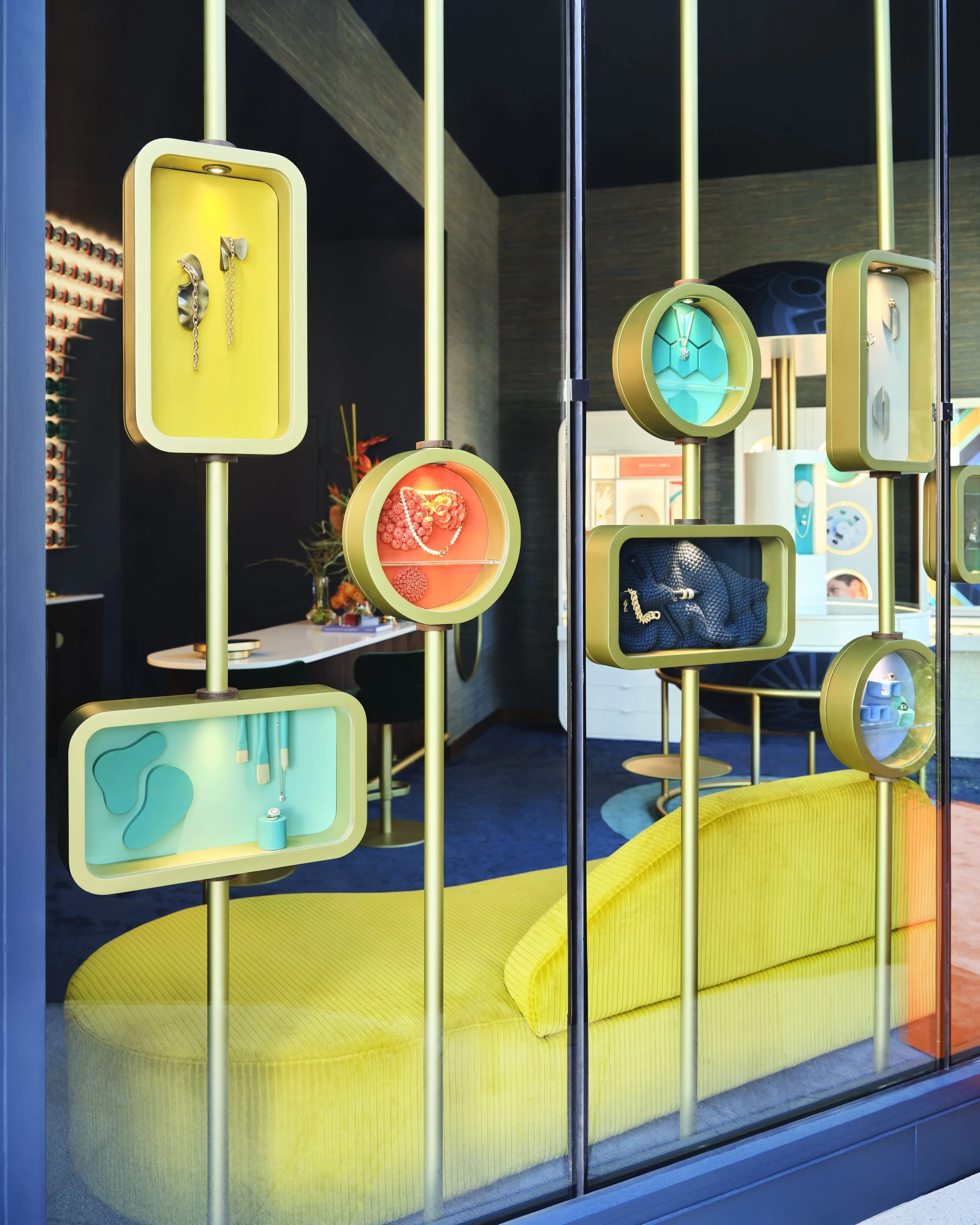 Display case with jewelry and accessories in a modern store, featuring yellow and turquoise accents and a padded yellow bench inside.