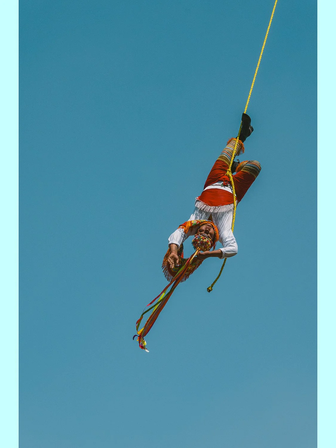 Unframed fine art photography print of a traditional Danza de los Voladores performer hanging upside down from a yellow rope against a vivid blue sky.