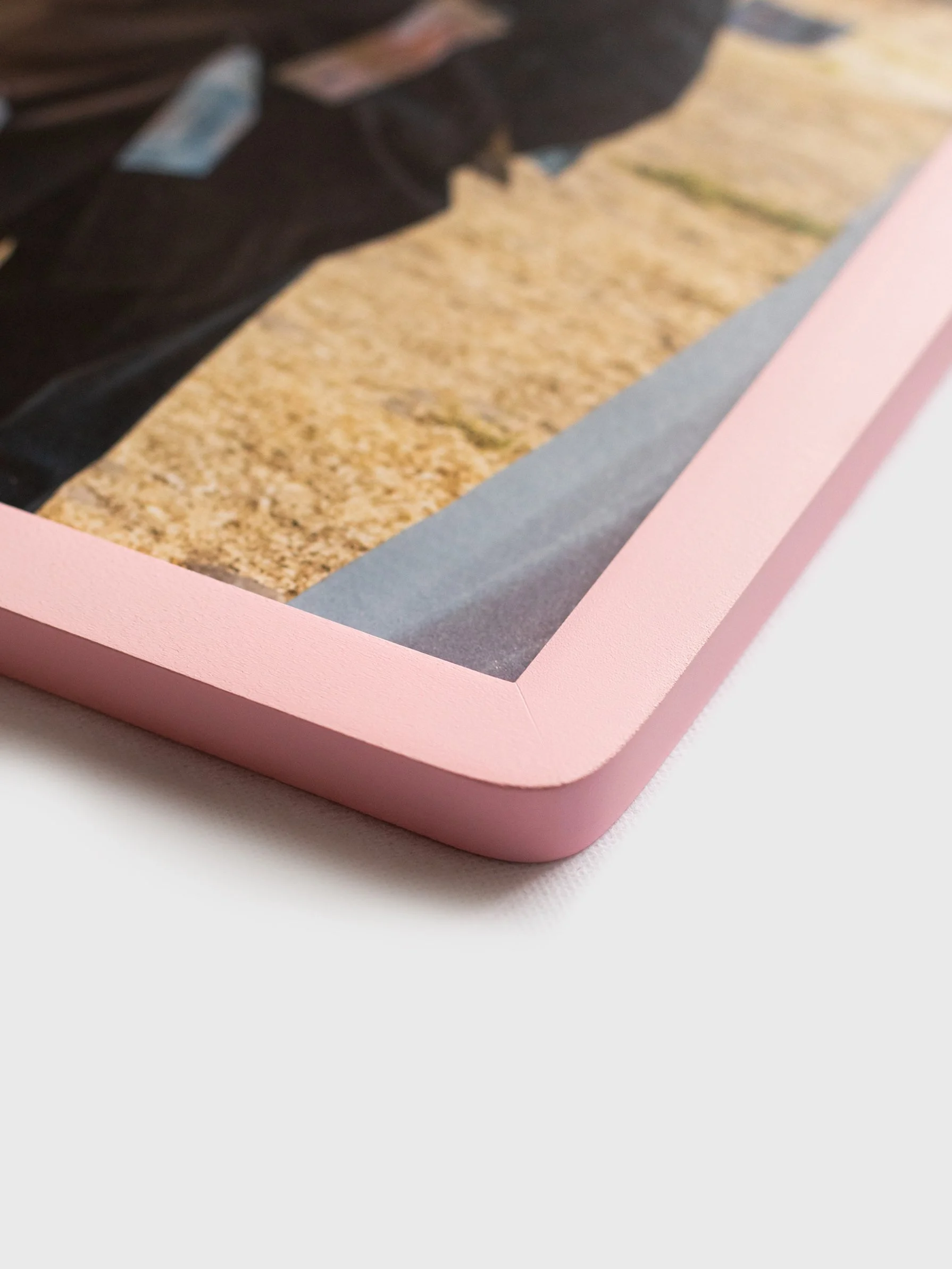 Close-up angled detail view of a handmade matte pink wooden picture frame showcasing the smooth rounded corners and premium flush-fit edge.