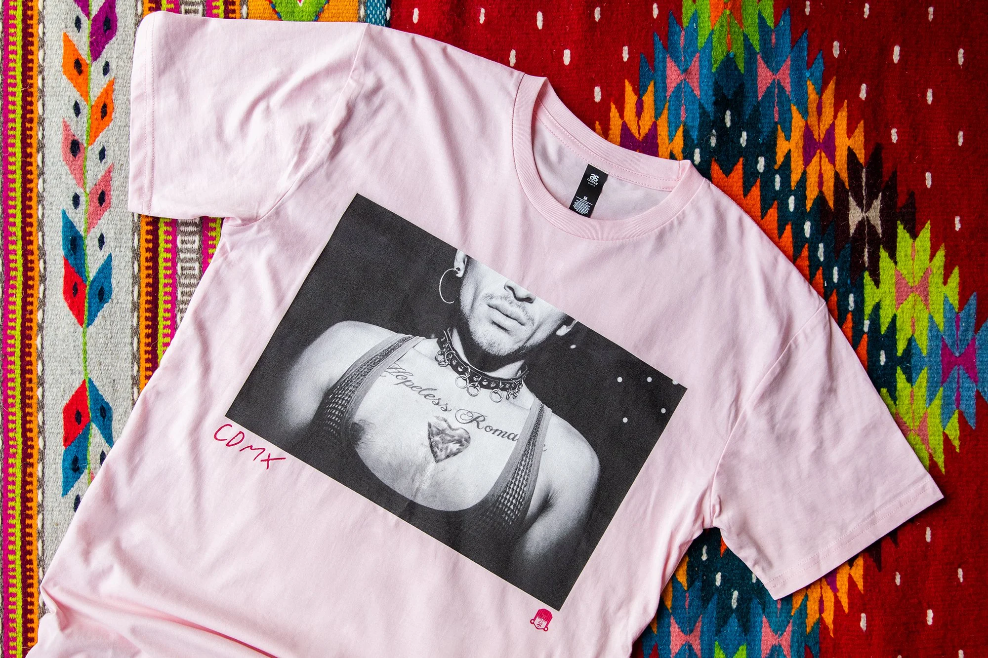 A pink graphic cotton t-shirt featuring a Mexico City street photography print, showcased flat on a handwoven Mexican textile.