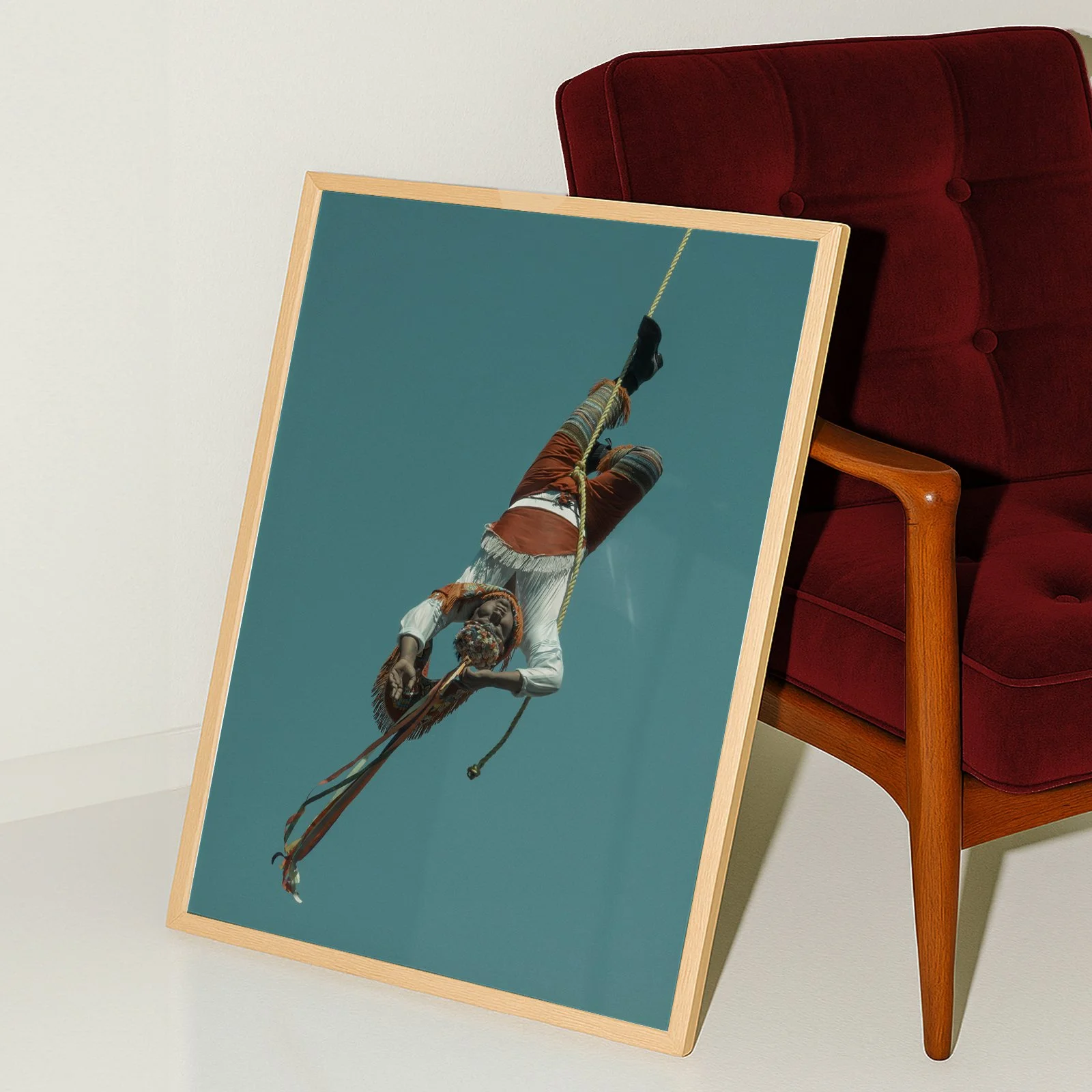 An art print of a trapeze artist hanging upside down from a rope, against a clear blue sky, leaning over the edge of a wooden-framed canvas.
