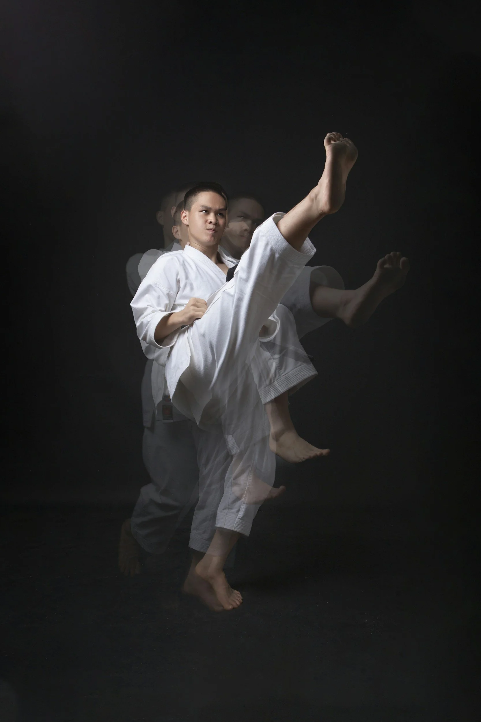 Stock image of a person in a white martial arts uniform performing a high kick, captured with motion blur against a black background.