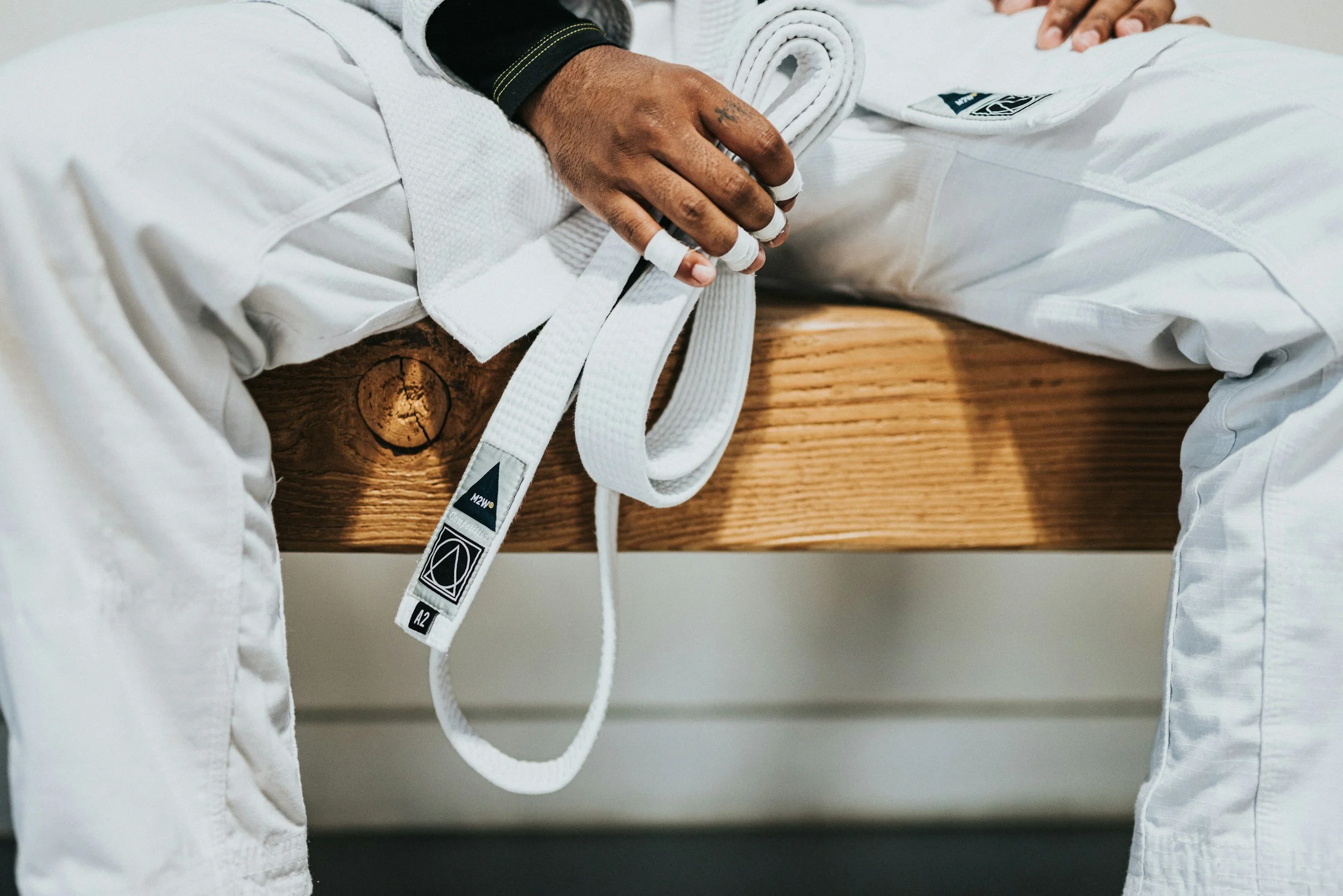 Stock image of a person wearing a white martial arts uniform, sitting with their hands clasped in their lap around a white belt that is untied.