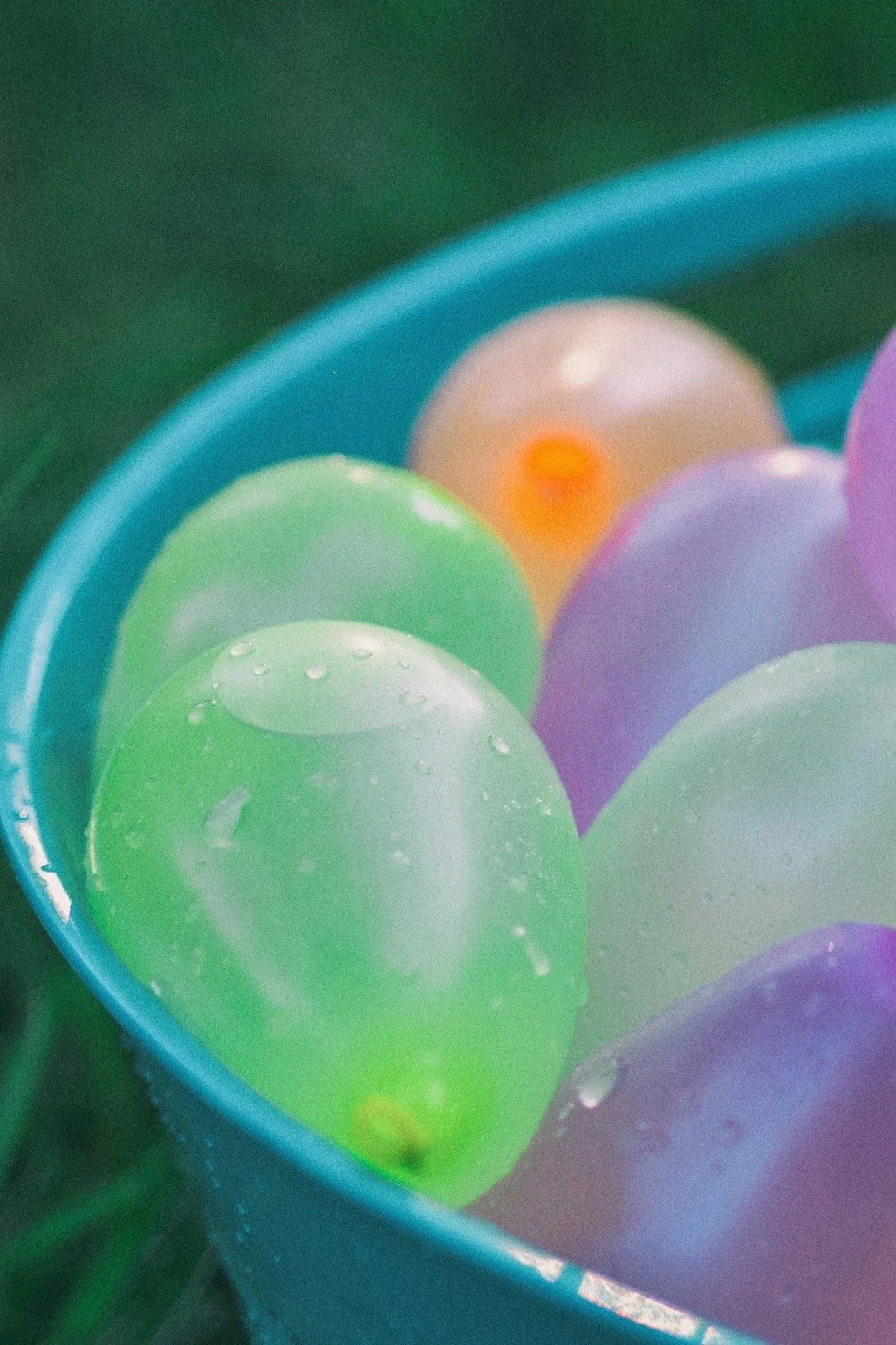 Stock image of colorful water balloons inside a blue container, with some water droplets visible on the surface of the balloons.