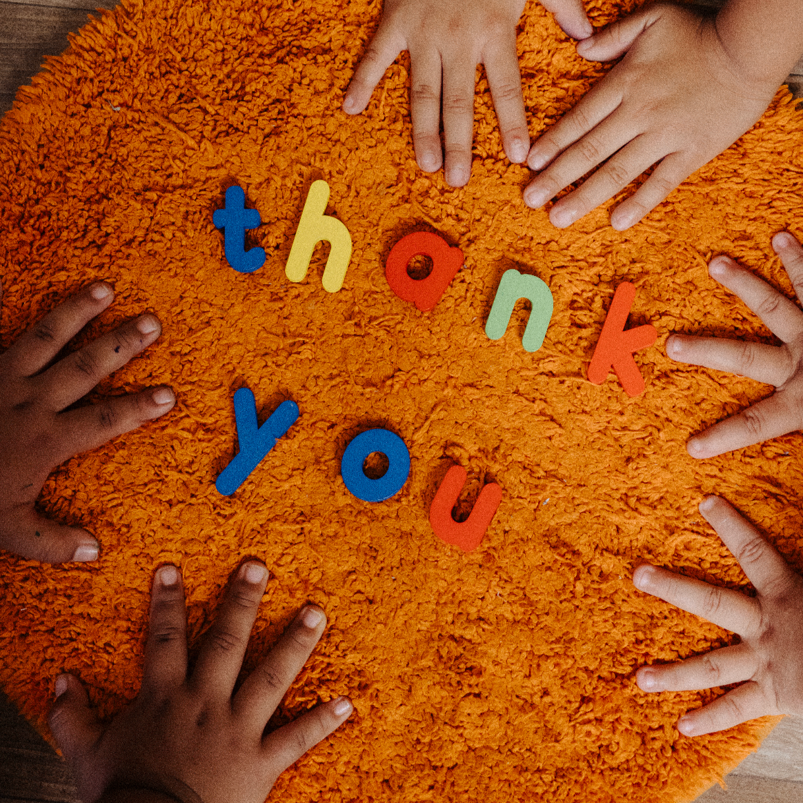 Multiple children’s hands placed around a fuzzy orange surface with colorful foam letters spelling out "thank you." Nonprofit in Guatemala, Villa Nueva, Photography, Videography, Content creation, social media management, website design for nonprofit