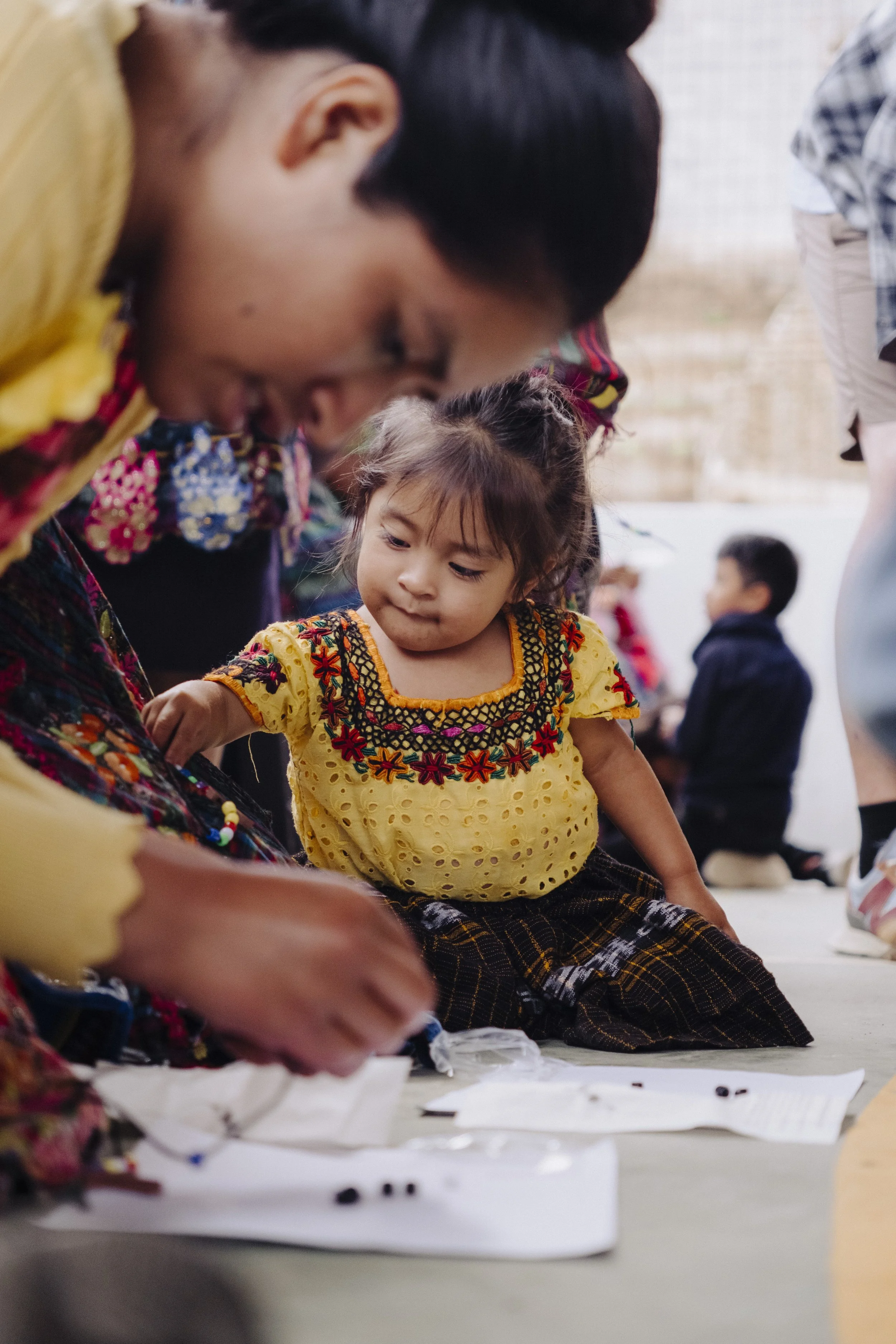A young guatemalan girl with traditional embroidered clothing sits on the ground. Cinematographer filming documentary interview | Video Production by Nonprofit Media Co.