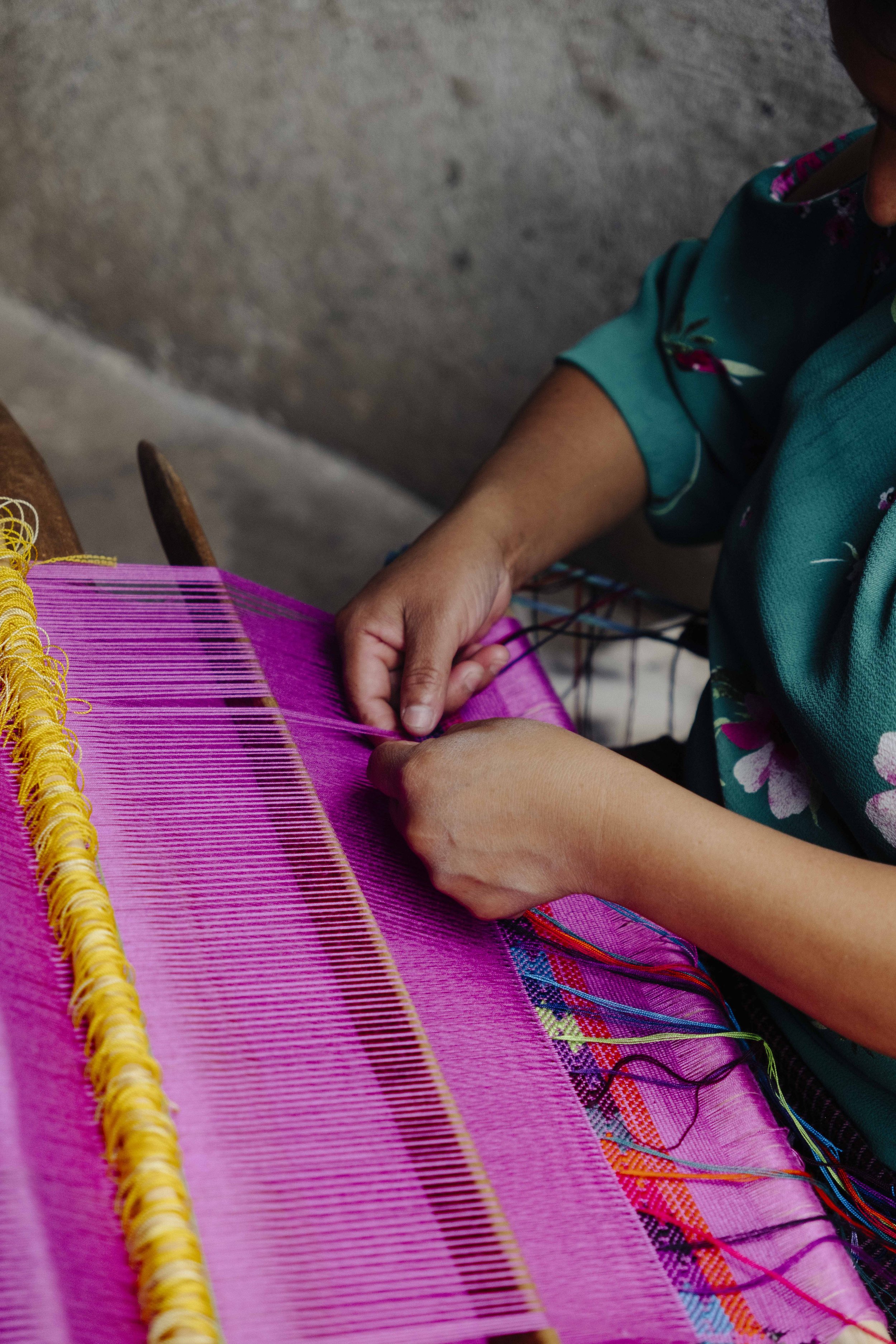 A person weaving a colorful textile using a loom, with vibrant pink threads in the foreground. Social empowerment in Rural Guatemala, Photography, Videography, Content creation, social media management, website design for nonprofit