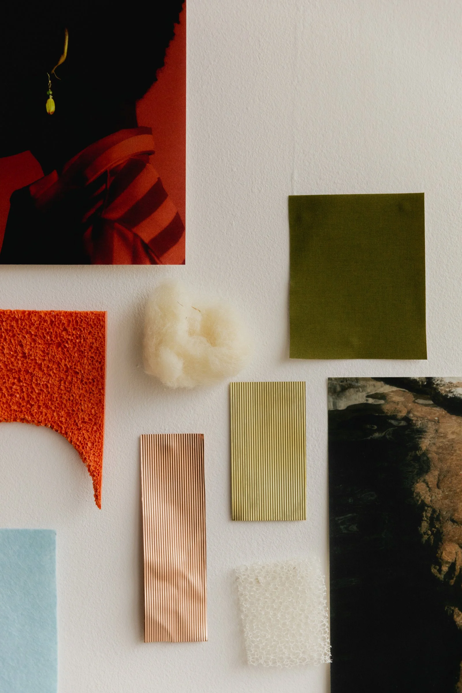 A wall with various textured and colored materials, including fabric, paper, and a photograph, arranged in a collage-style display.