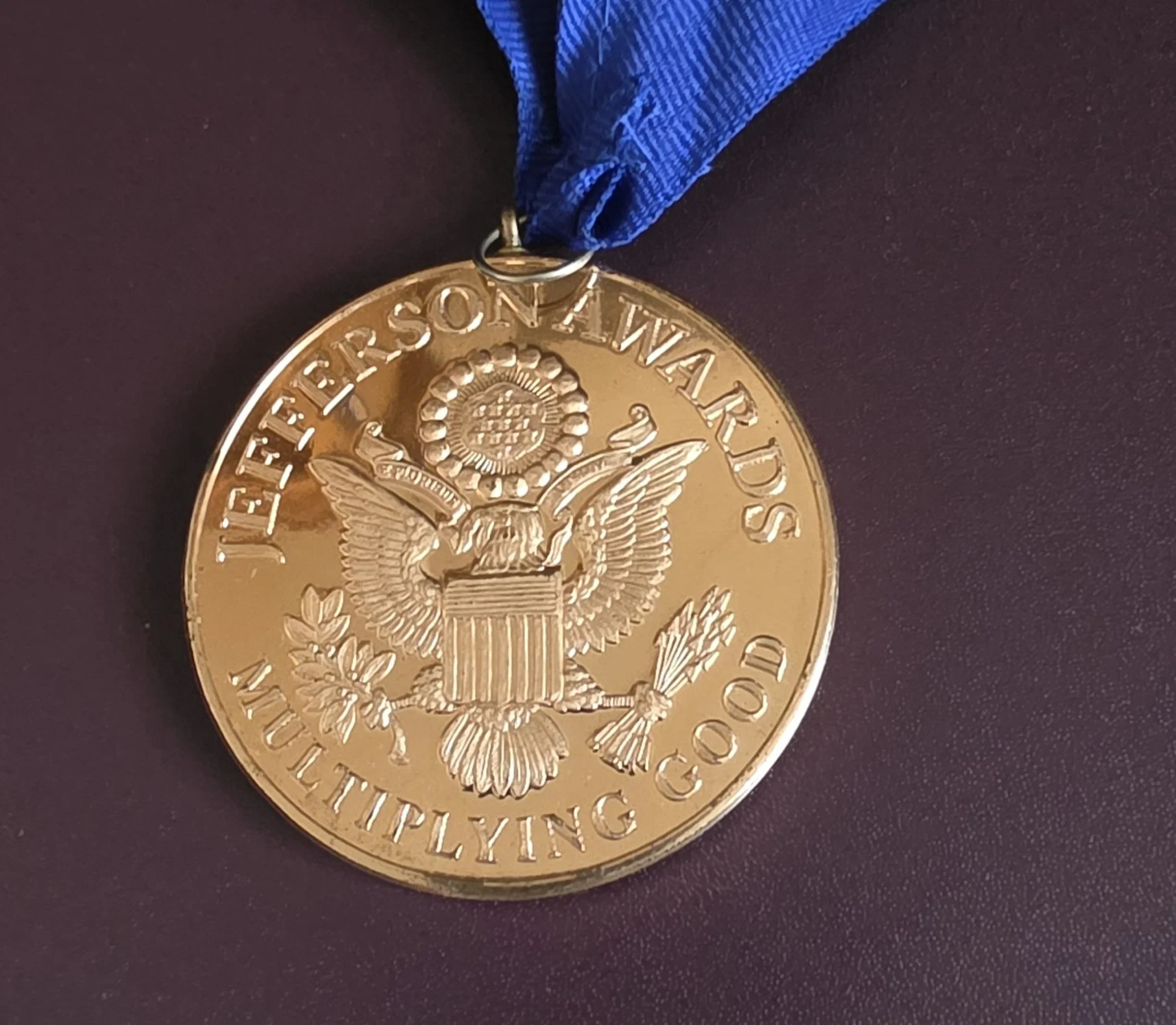 Gold medal with embossed eagle and text, attached to a blue ribbon.
