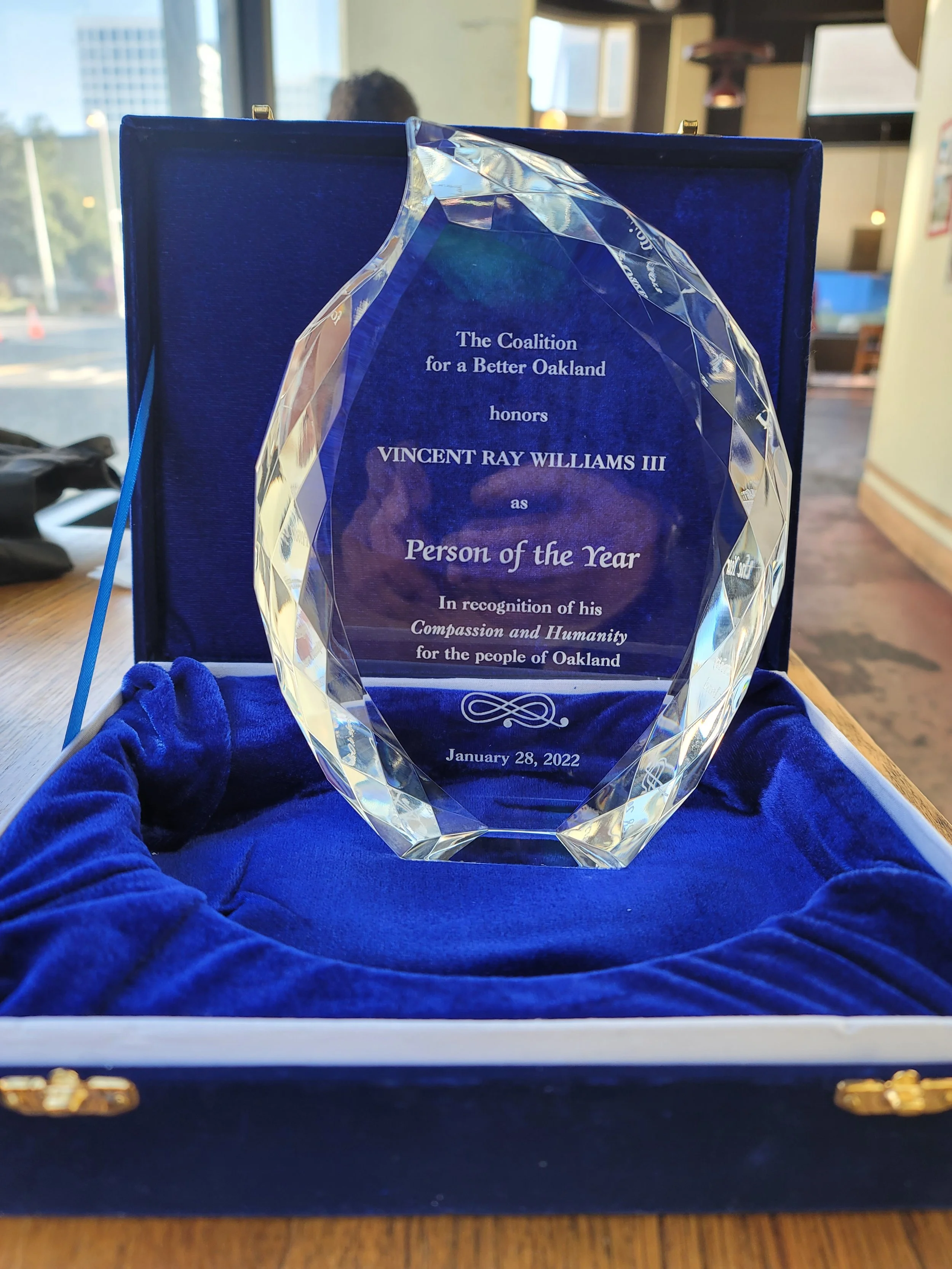 An award engraved with the text, 'The Coalition for a Better Oakland honors Vincent Ray Williams III as Person of the Year, in recognition of his Compassion and Humanity for the people of Oakland, January 28, 2022,' is displayed inside a blue velvet-lined box.