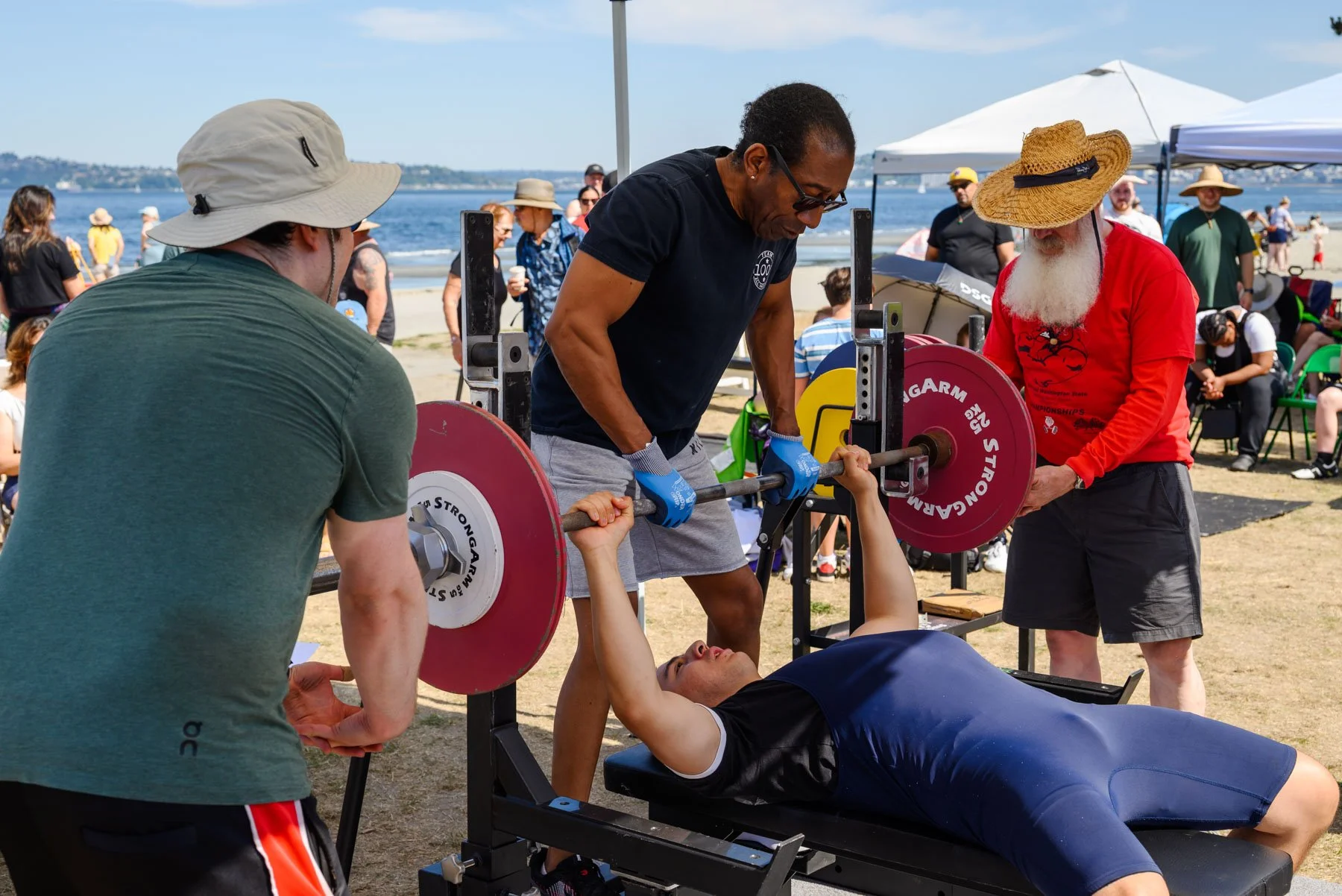 Trainers spotting someone doing chest press at Alki Beach powerlifting competition