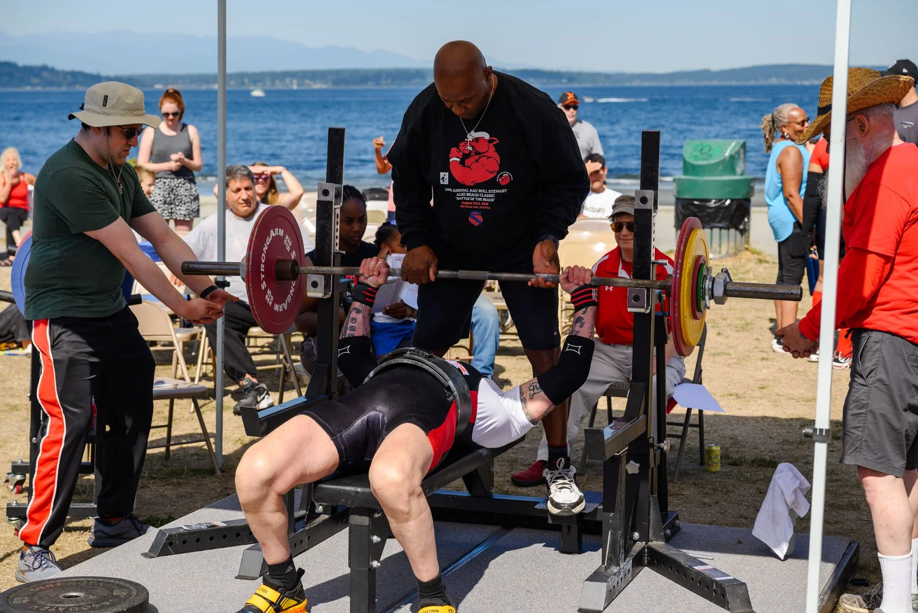 Bull and two trainers spotting competitor doing a chest press at Alki Beach powerlifting competition